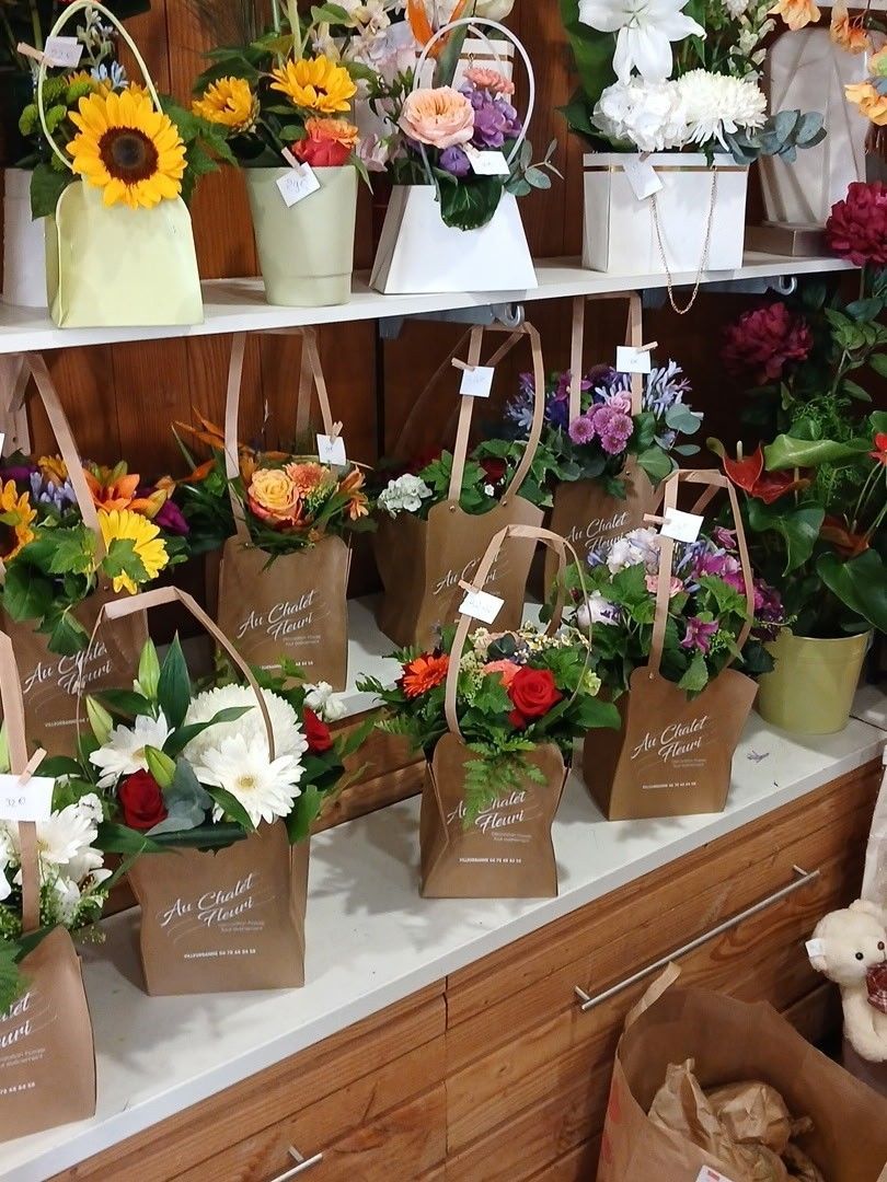 Des bouquets de fleurs et des compositions en pot, avec des tournesols et des fleurs variées, sont exposés sur les étagères d'un magasin.