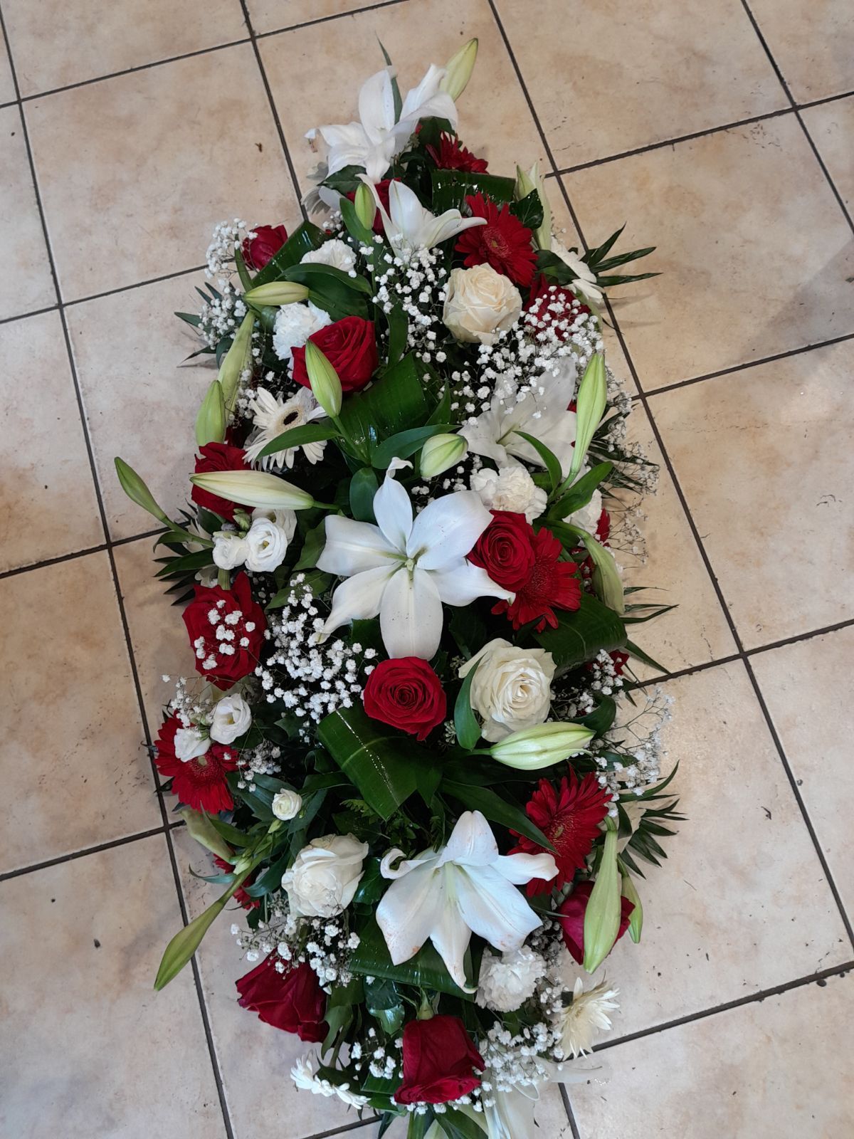 Dessus de cercueil avec des roses rouges et blanches ainsi que d'autres fleurs