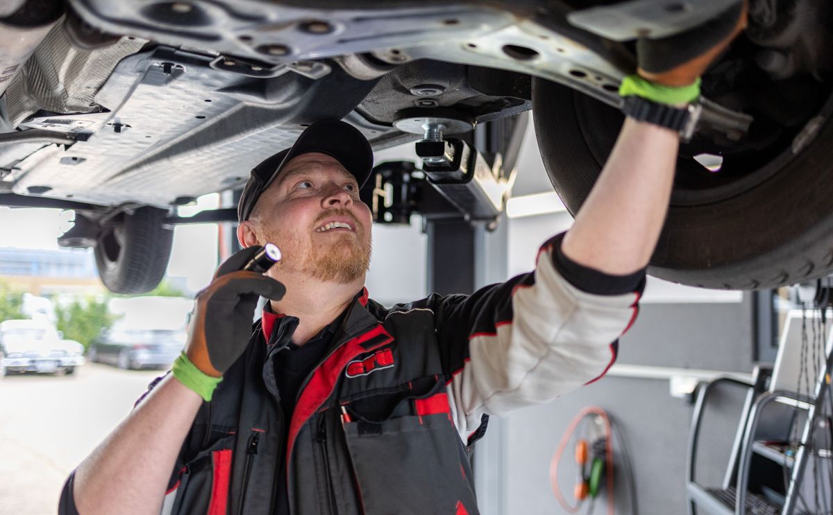 Mechaniker überprüft in einer Werkstatt einen Automotor mit einer Taschenlampe; konzentrierter Gesichtsausdruck.