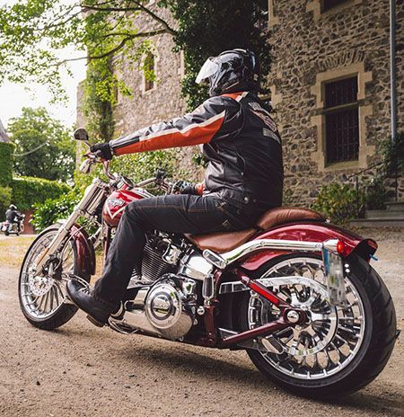 Mann auf einem roten Harley-Davidson-Motorrad, das vor einem Steingebäude geparkt ist.