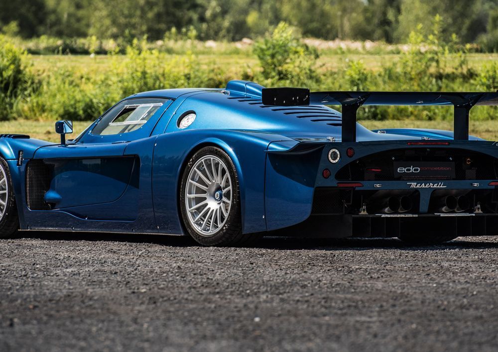 Blauer Maserati MC12-Rennwagen auf einer Schotterstraße, mit großem Heckflügel und seitlichen Lufteinlässen.