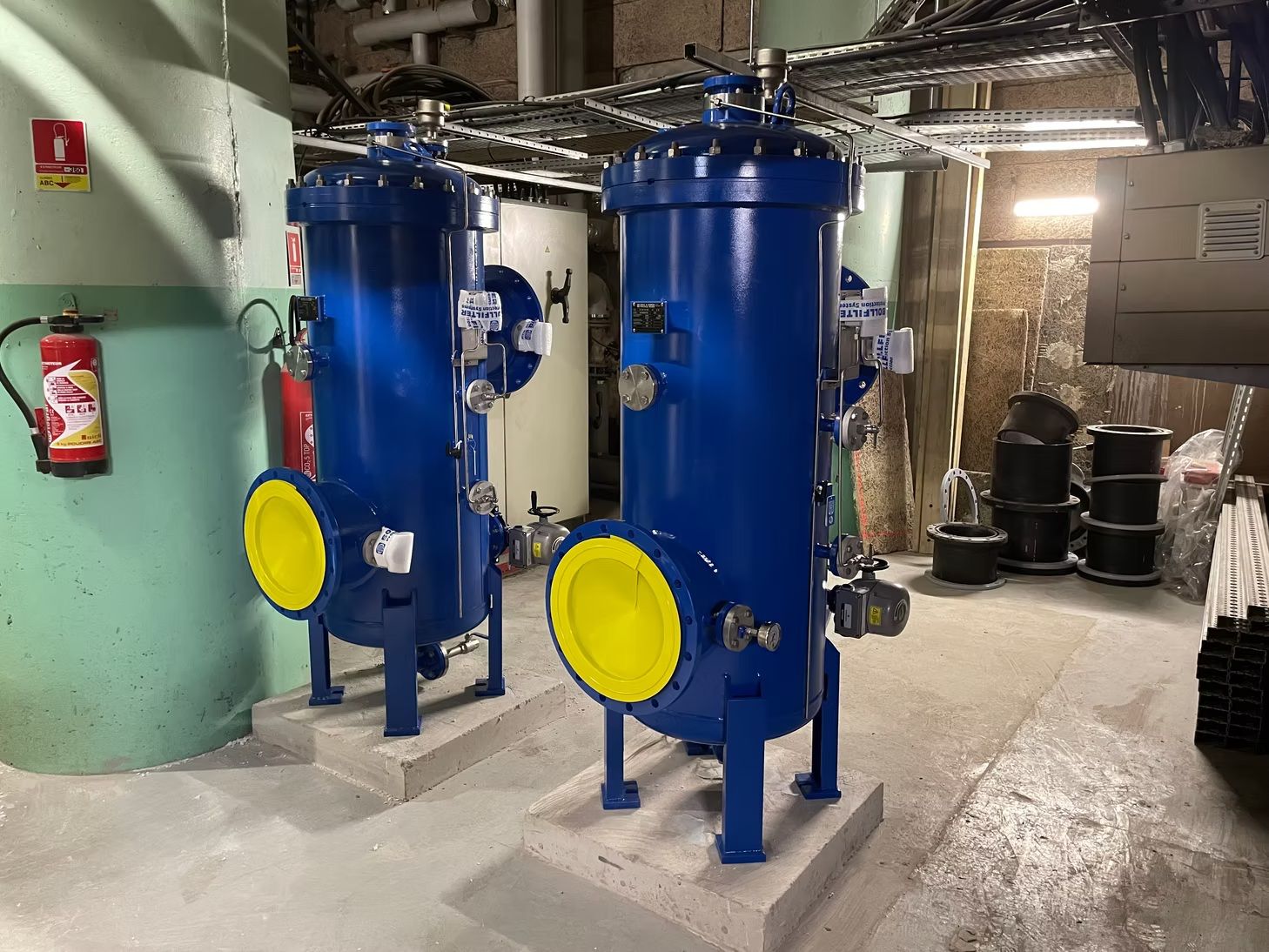 Cuves industrielles bleues avec trappes d’accès jaunes dans un local technique en sous-sol
