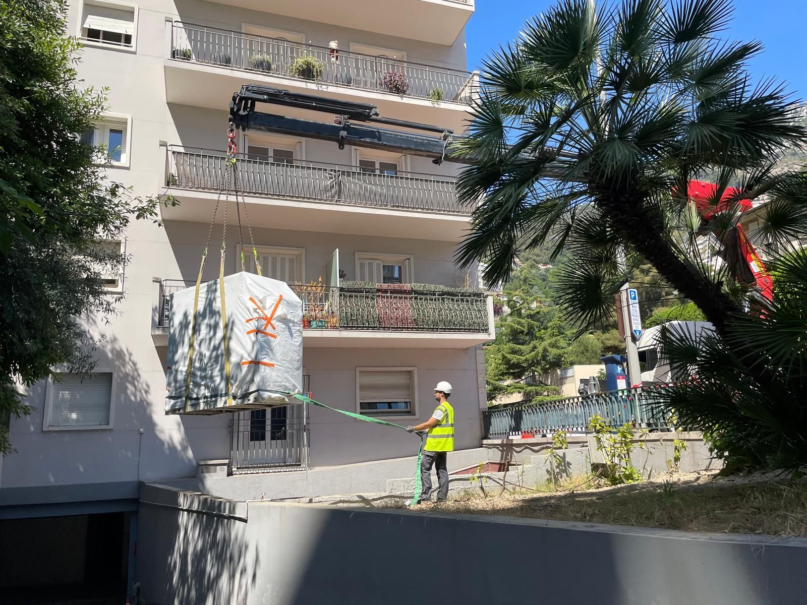 Immeuble résidentiel avec balcons, palmiers et un ouvrier en gilet fluo dans une rue ensoleillée
