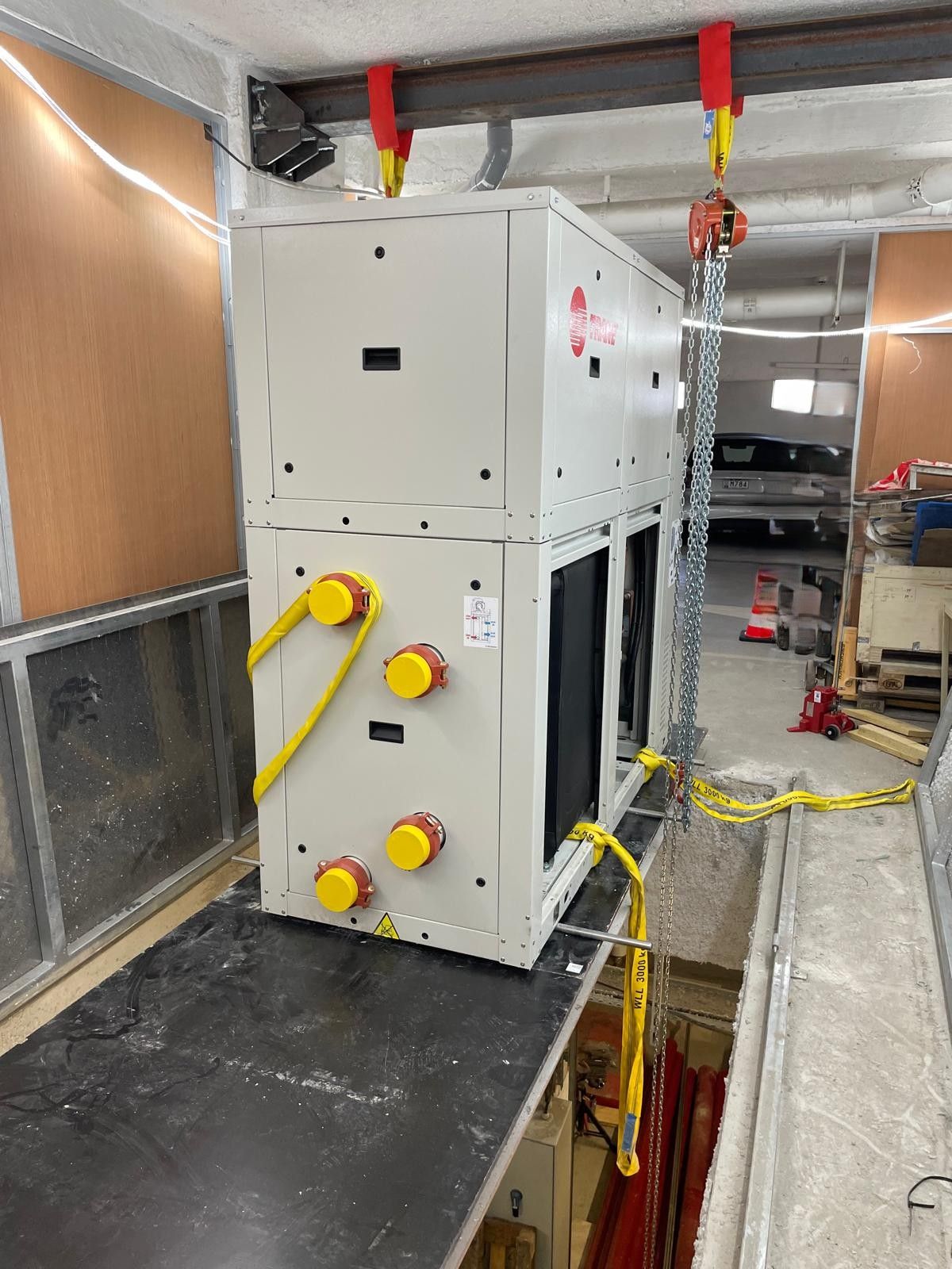 Grande unité de CVC blanche dans un couloir de chantier, avec des poignées jaunes et des sangles de levage rouges suspendues au-dessus.