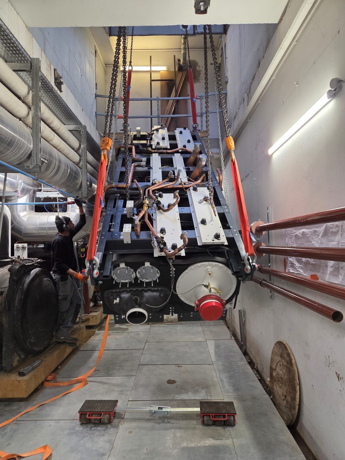 Grande machine déplacée dans un étroit couloir industriel à l’aide de sangles de levage orange et de rails