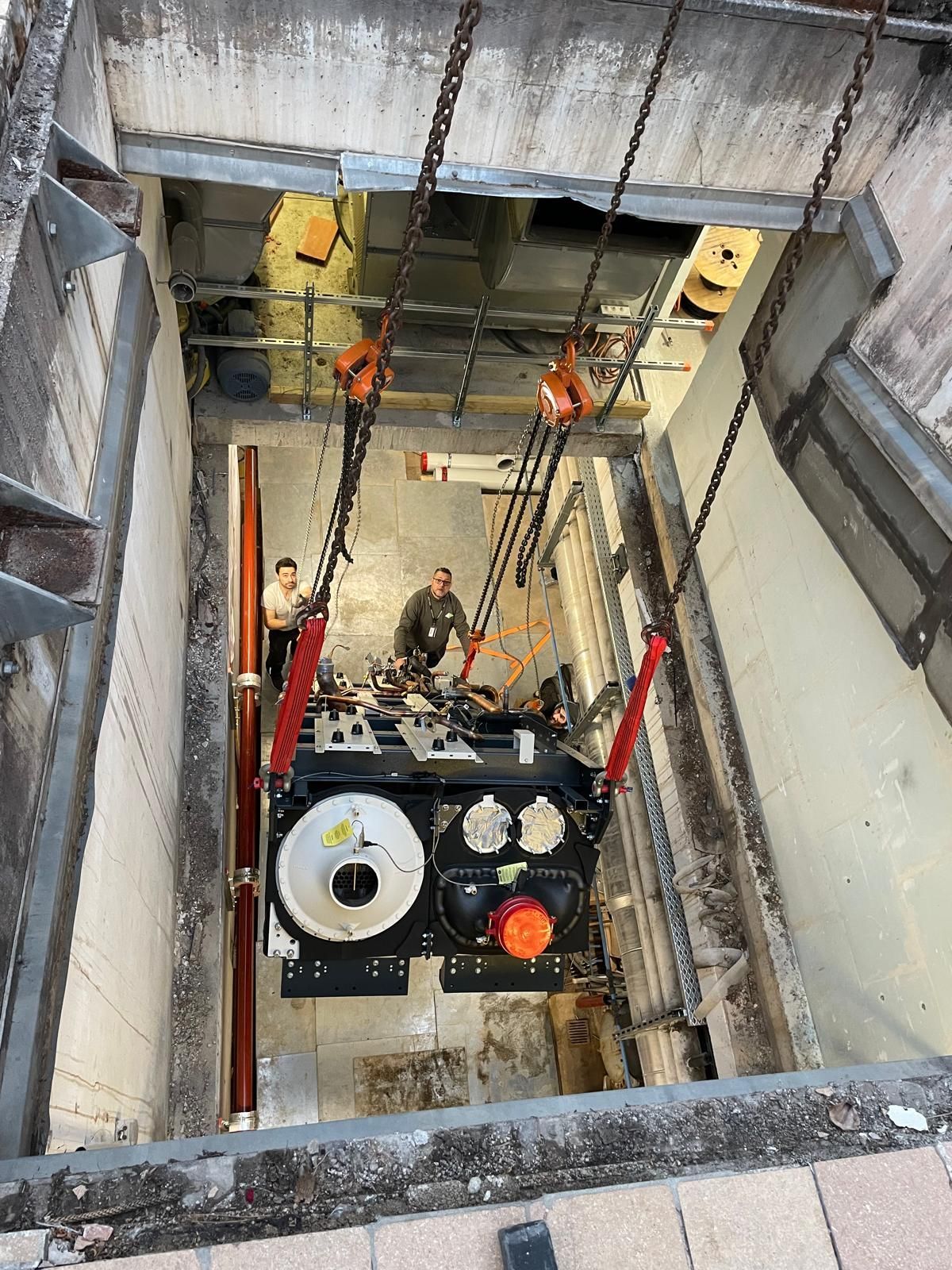 Puits de chantier avec des ouvriers et des machines, vu d’en haut, avec des rails et des câbles rouges.