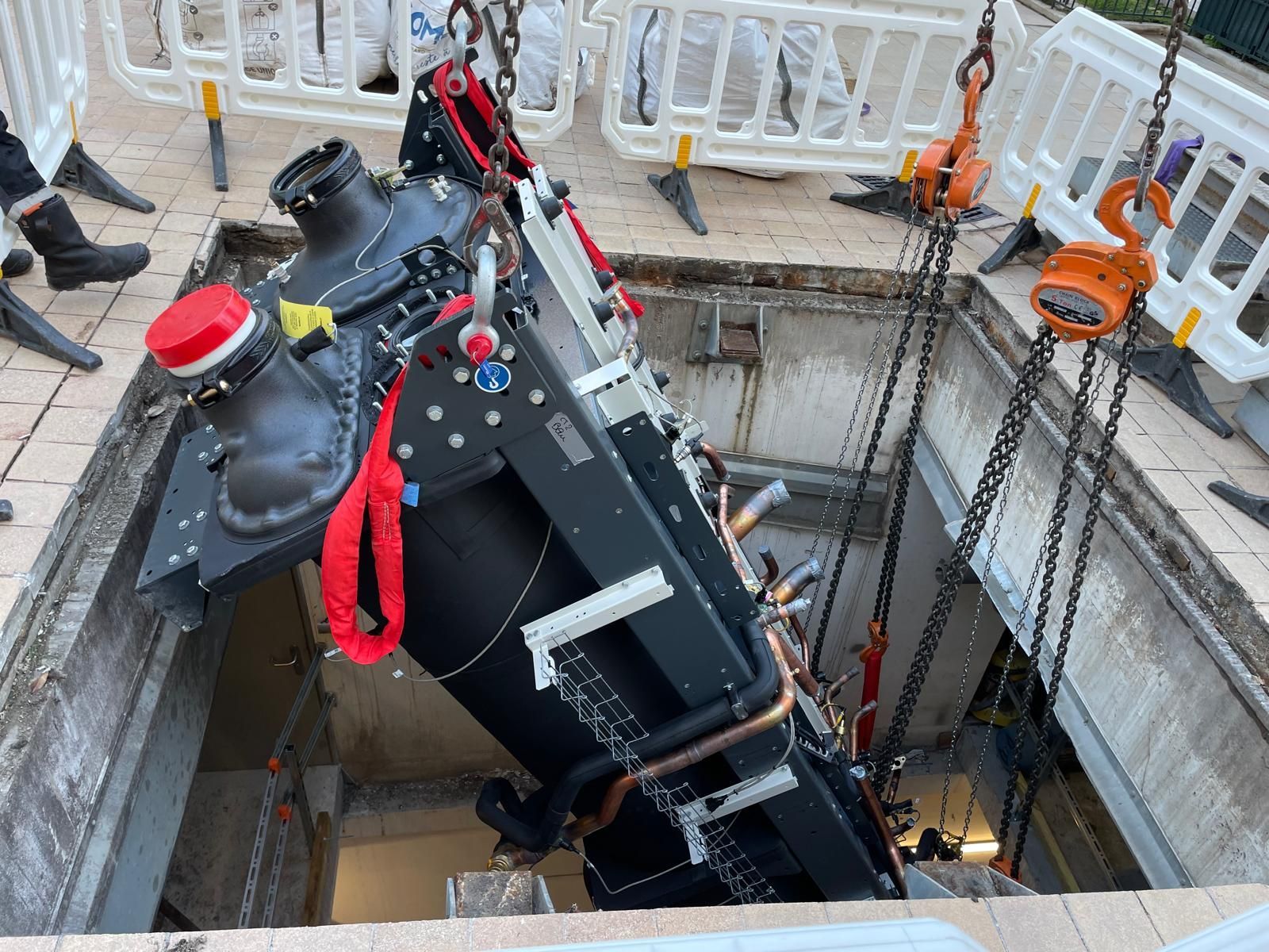 Une machine industrielle noire descendue à l’aide de chaînes dans une fosse en béton sur un chantier.