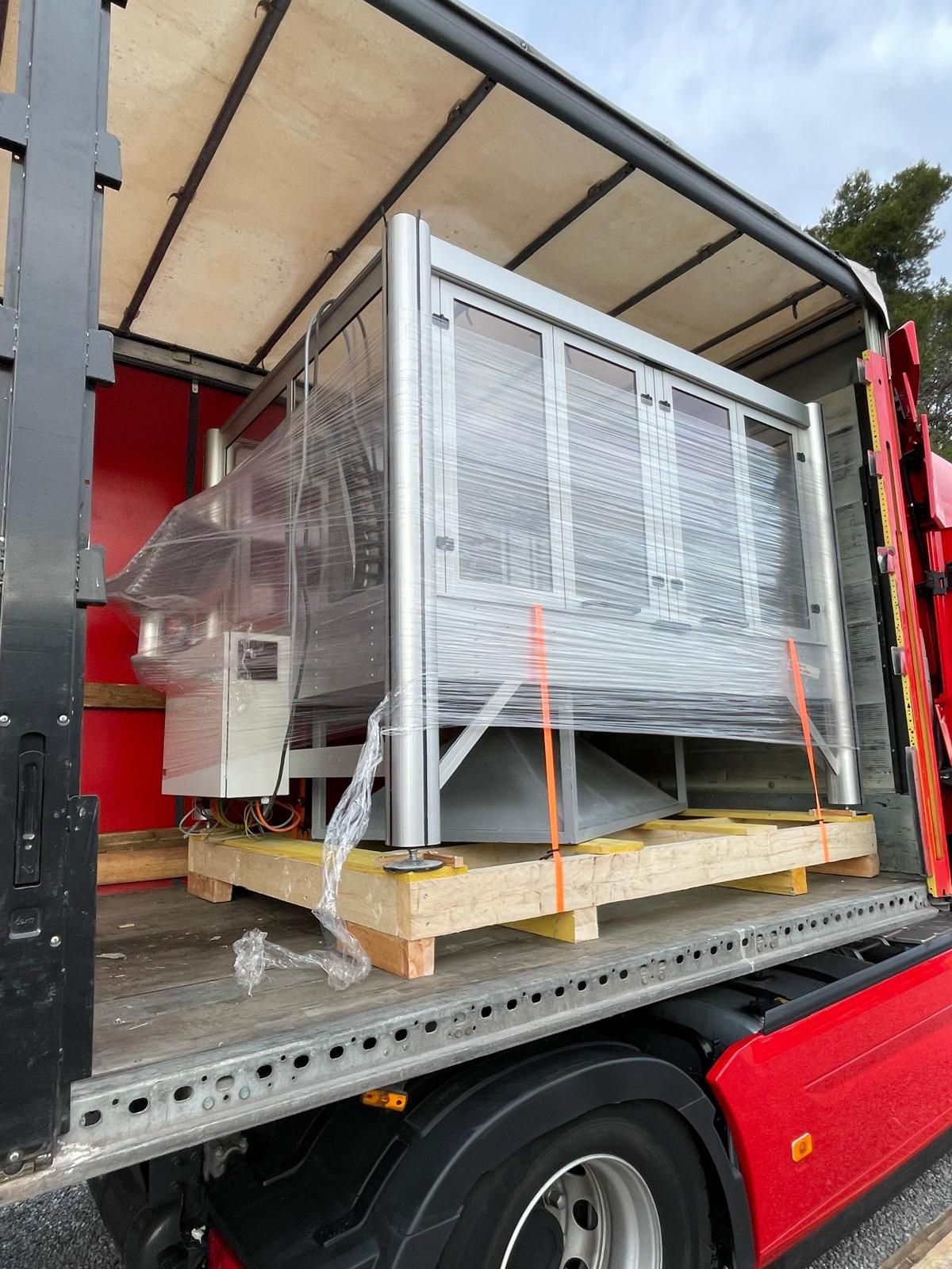 Grande machine emballée et sanglée sur une palette, à l’intérieur de l’espace de chargement d’un camion de livraison rouge