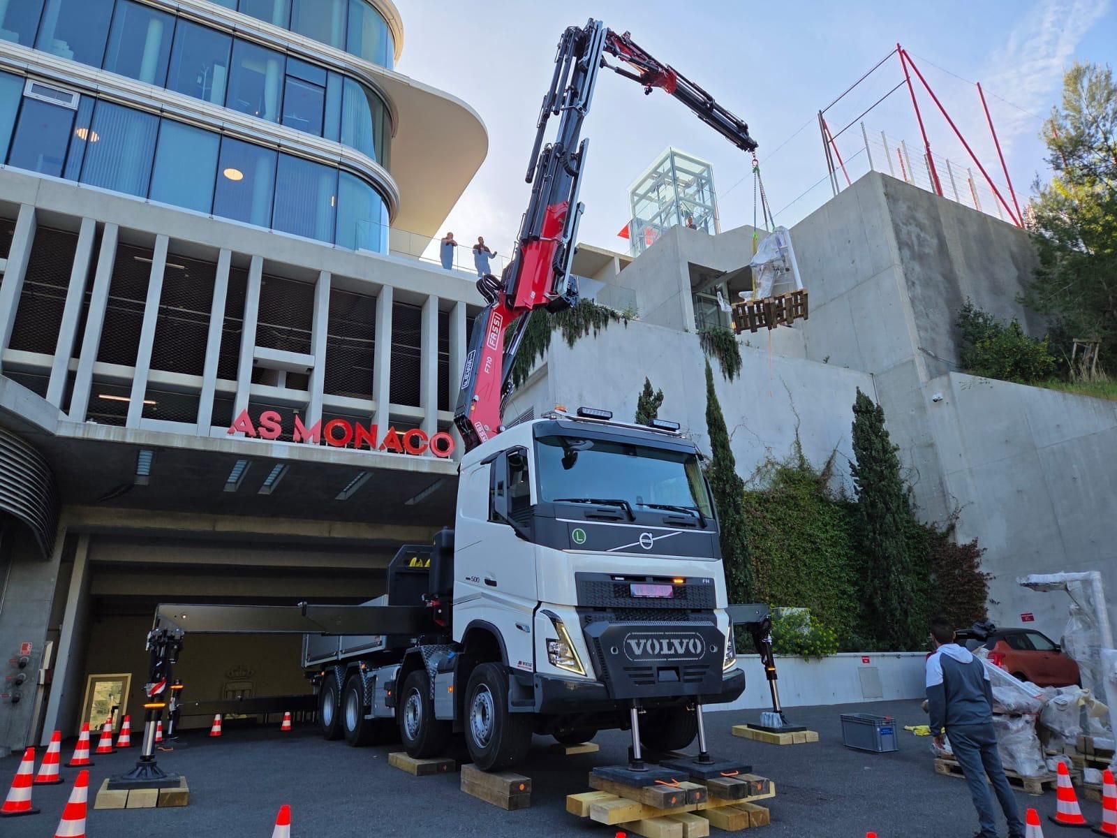 Camion utilitaire blanc sous une grue, sur un chantier à côté d’un bâtiment moderne