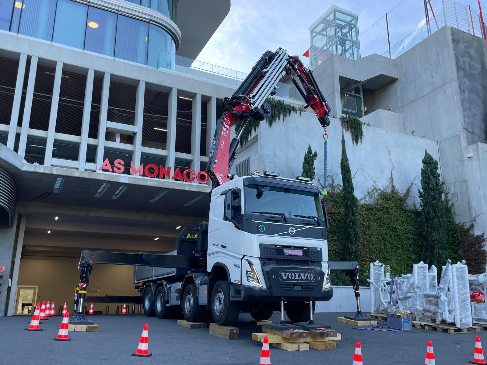 Un camion-grue soulève des débris devant l’entrée d’un bâtiment, avec des cônes orange et des barrières de chantier