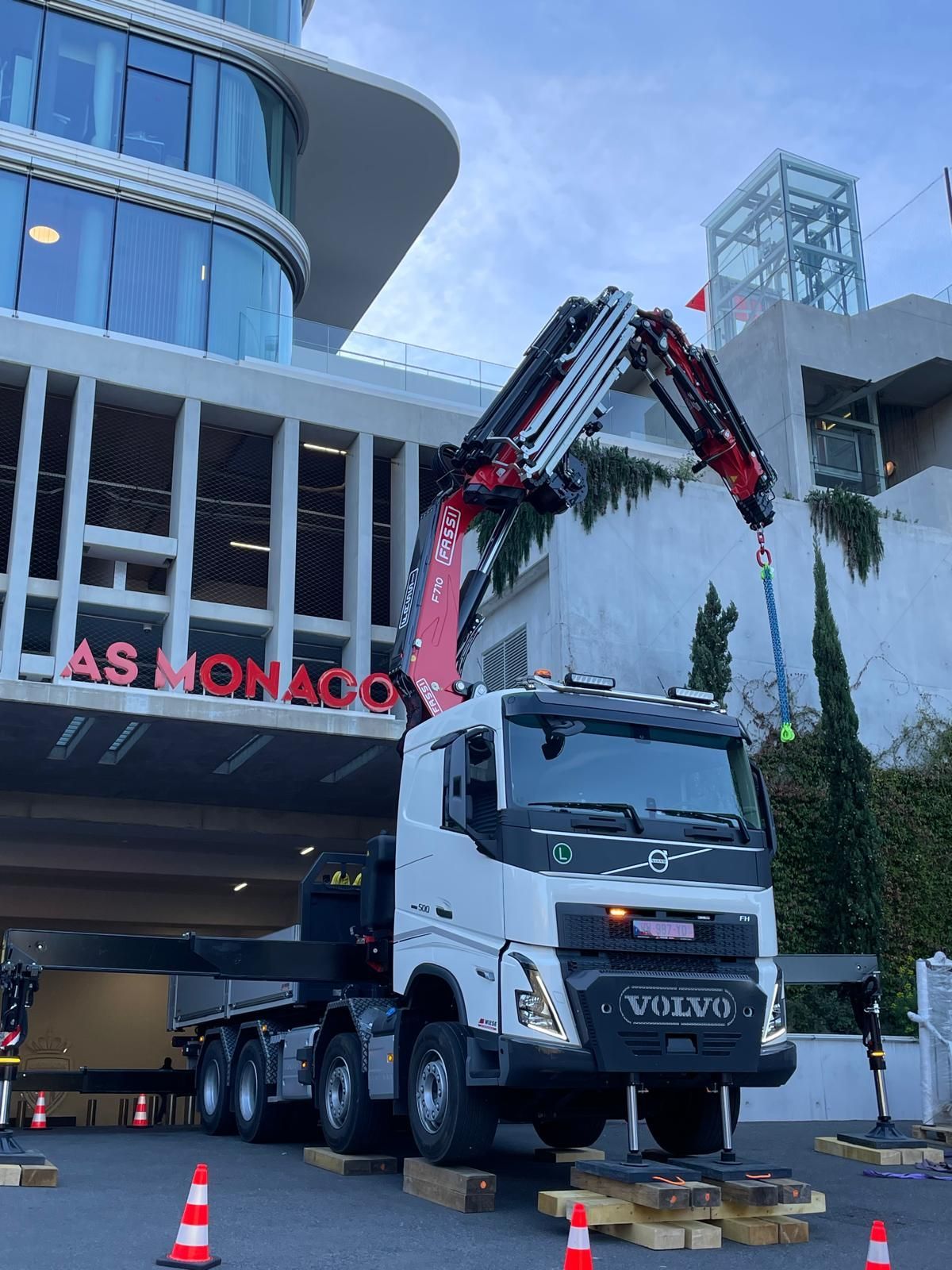 Un camion-grue soulève une grande plateforme à côté d’un immeuble moderne portant l’inscription « AS MONACO »