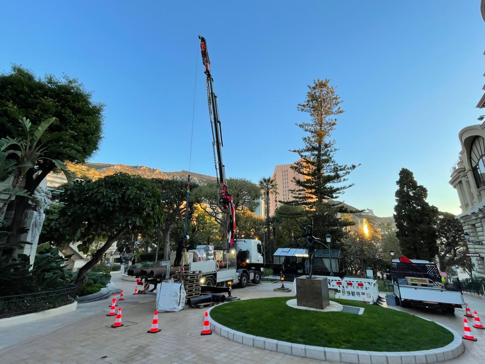 Esplanade extérieure avec une grue, des cônes orange et des arbres au coucher du soleil sous un ciel bleu dégagé