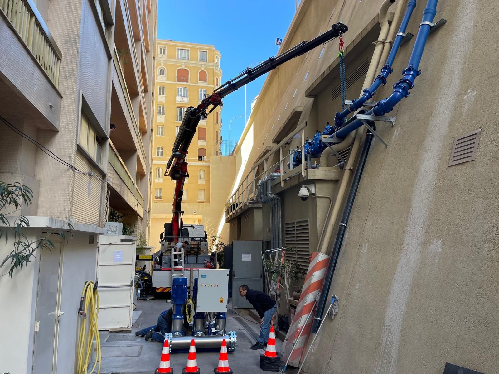 Une équipe de chantier utilise une grue pour déplacer des matériaux entre des bâtiments dans une ruelle étroite