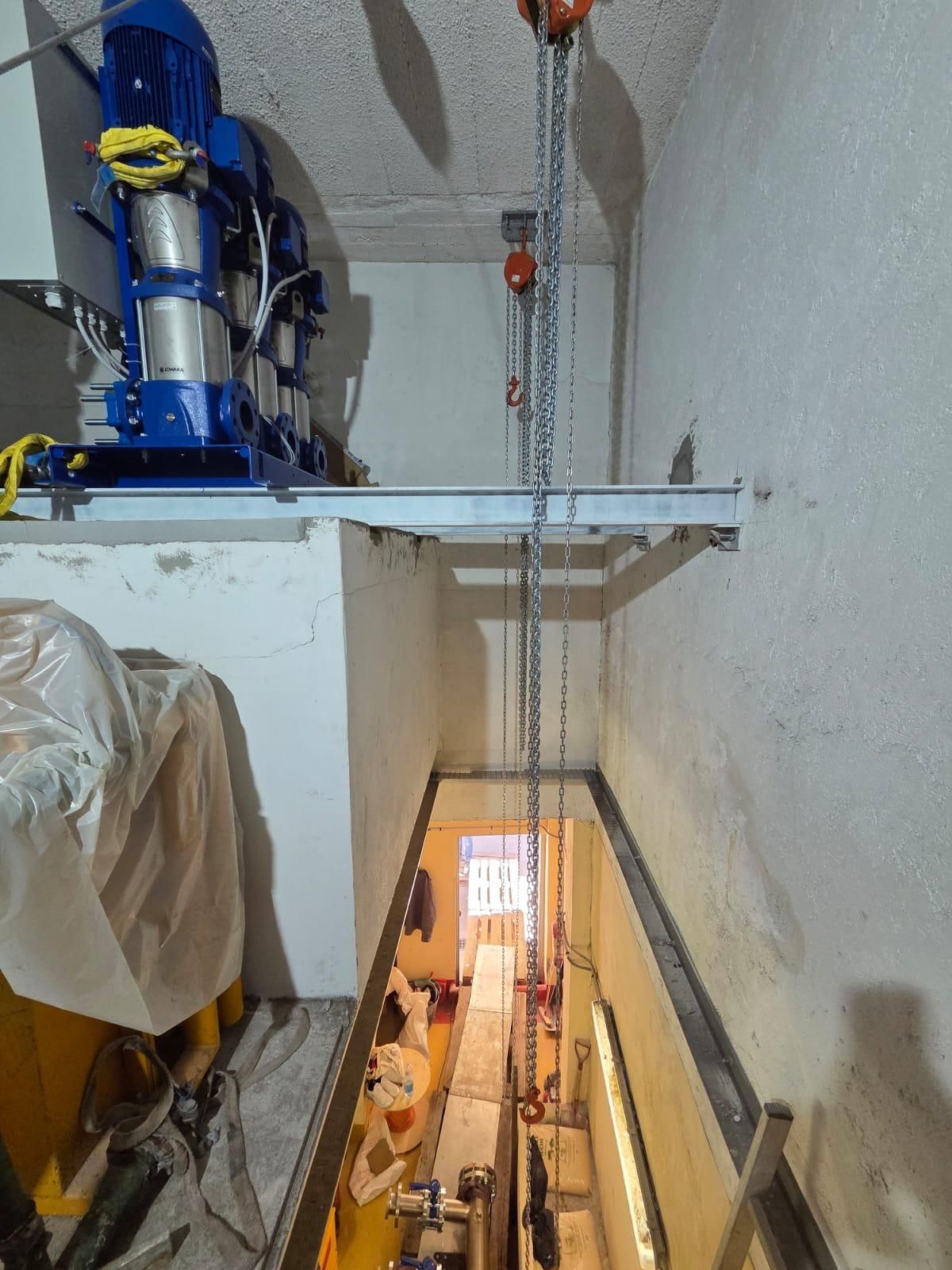 Puits industriel avec un palan à chaîne suspendu au-dessus d’une ouverture étroite dans une pièce aux murs blancs