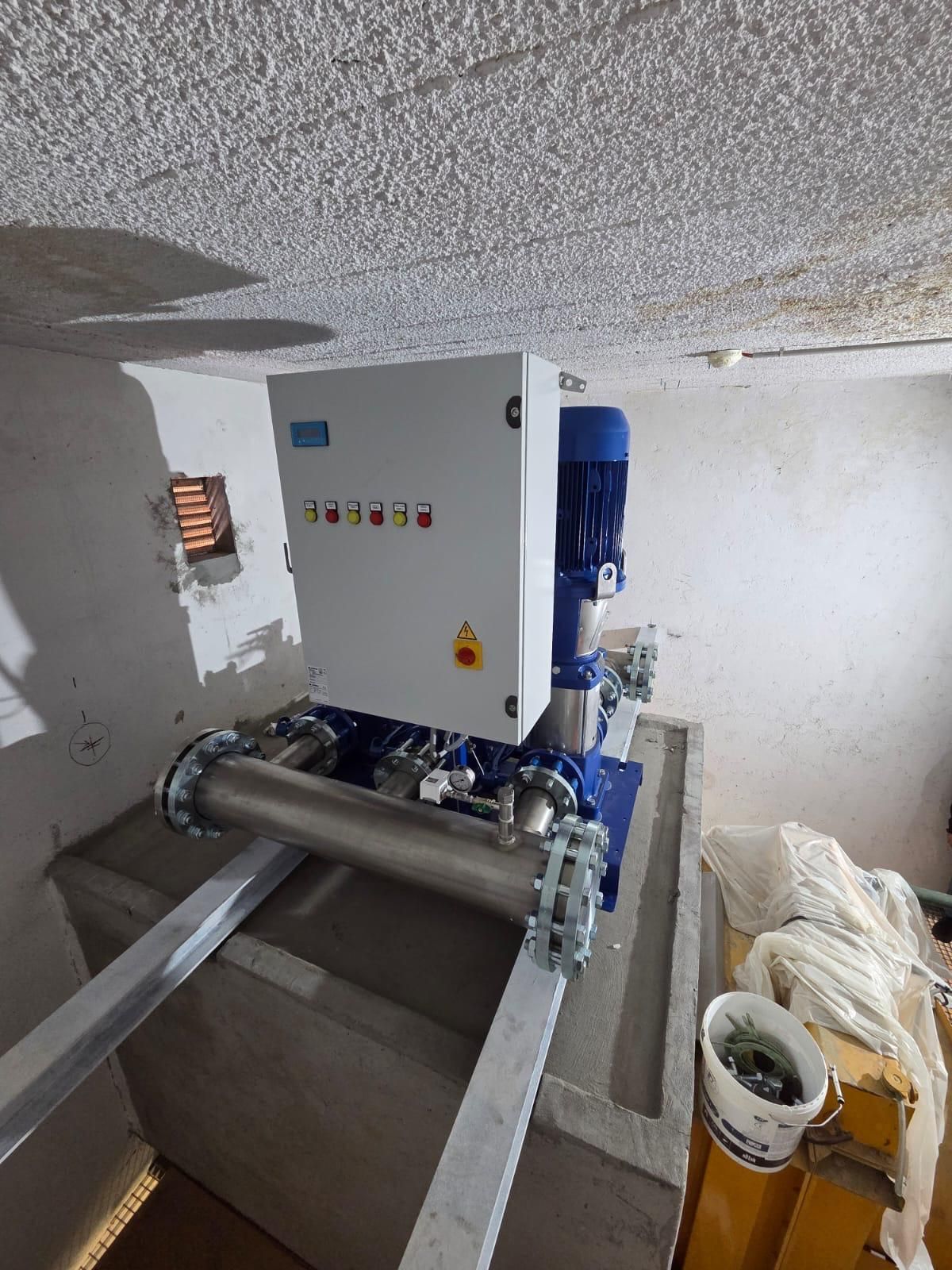 Machines industrielles dans une pièce en béton, avec un coffret de commande, des tuyaux et des composants bleus.