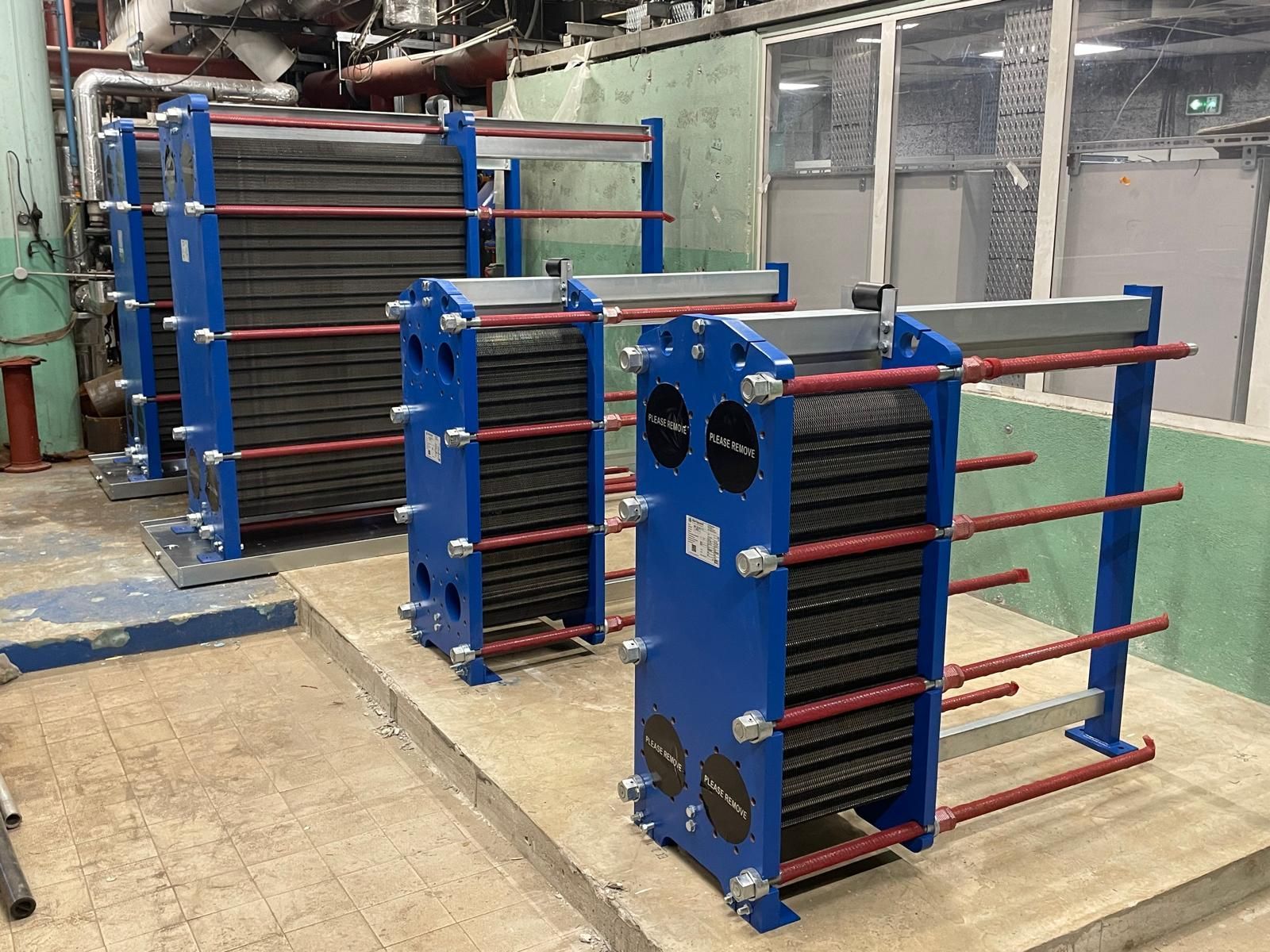 Échangeurs thermiques industriels bleus empilés dans un atelier d’usine, avec des tiges de support rouges et des tuyaux métalliques.