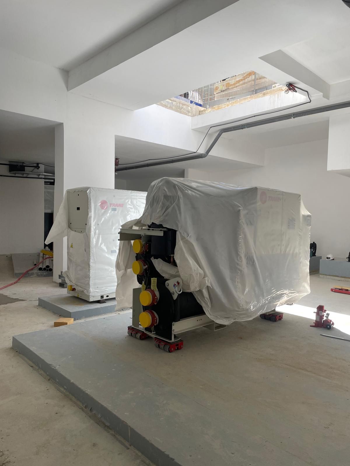 Machines couvertes dans une salle industrielle lumineuse dotée d’un puits de lumière et d’un sol en béton.