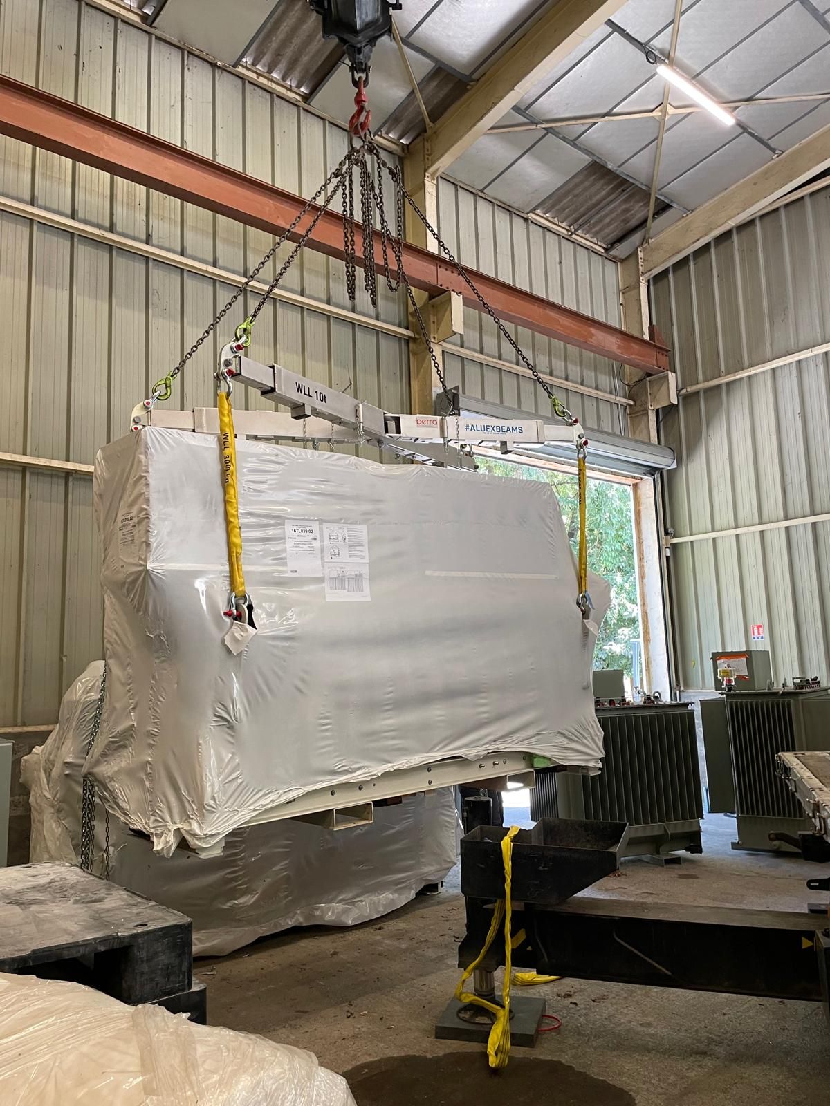 Une grande machine industrielle emballée, soulevée par une grue dans un atelier-entrepôt