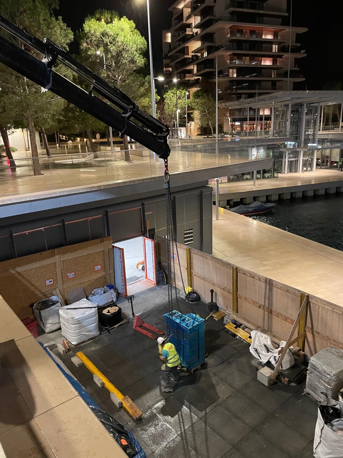 Chantier de nuit au bord d’un canal, avec des engins et des barrières sous un éclairage puissant.