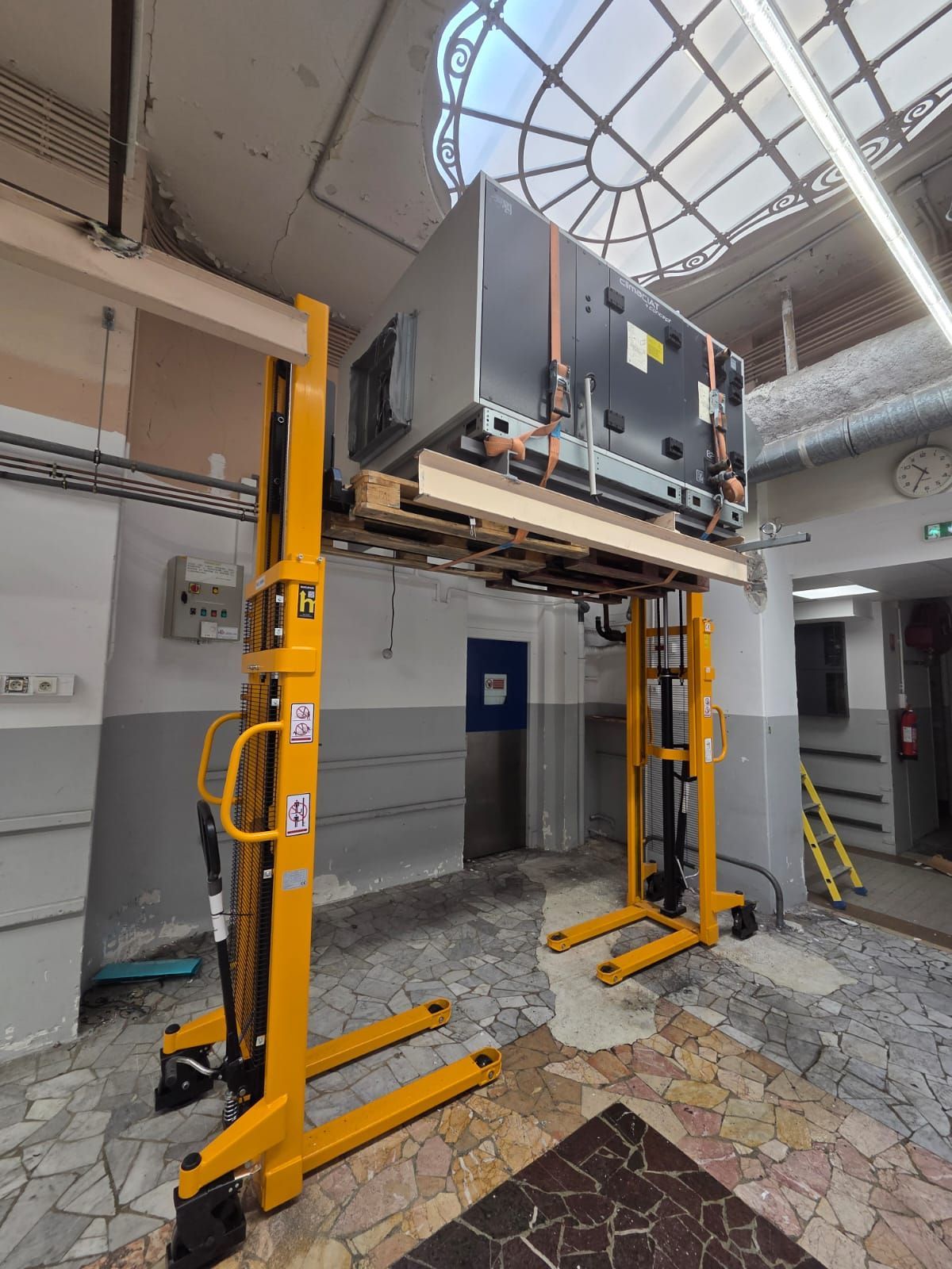 Gros appareil électroménager soulevé par des crics hydrauliques jaunes dans le hall d’un bâtiment endommagé