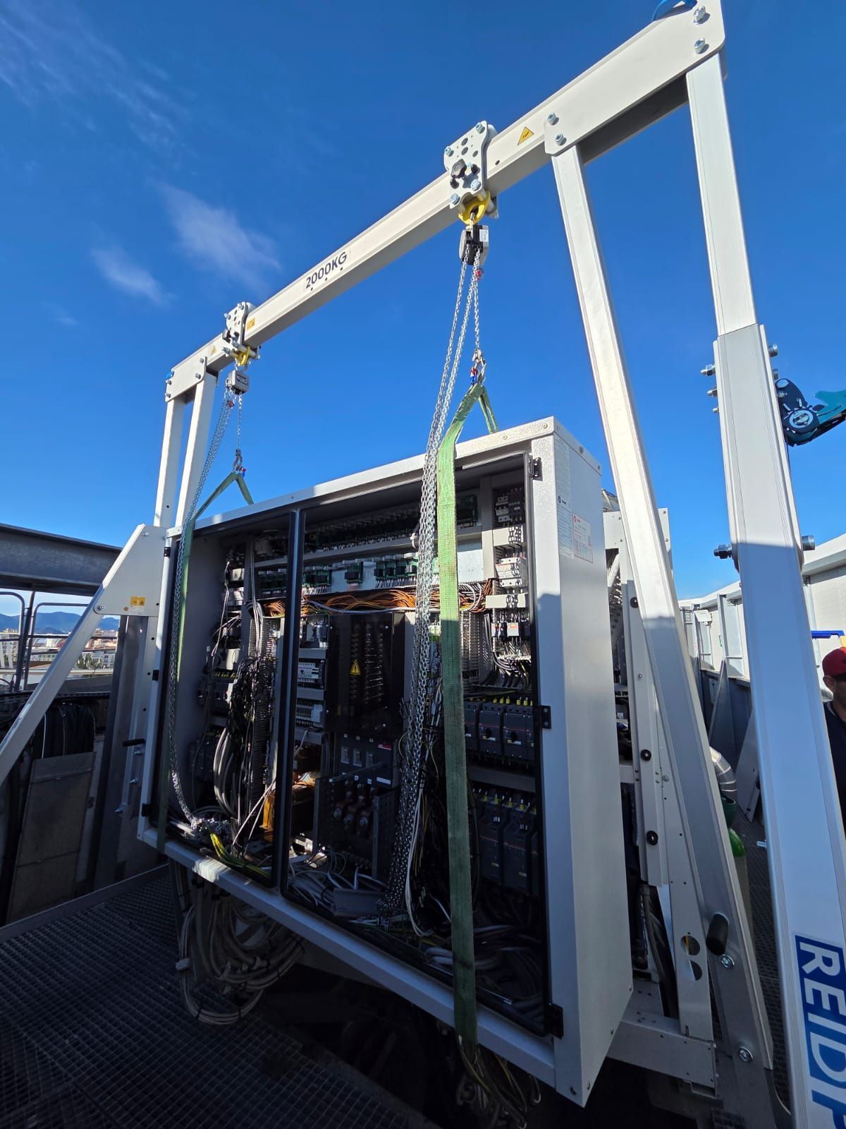 Grue soulevant une baie ouverte avec des câbles et des équipements électroniques sur fond de ciel bleu