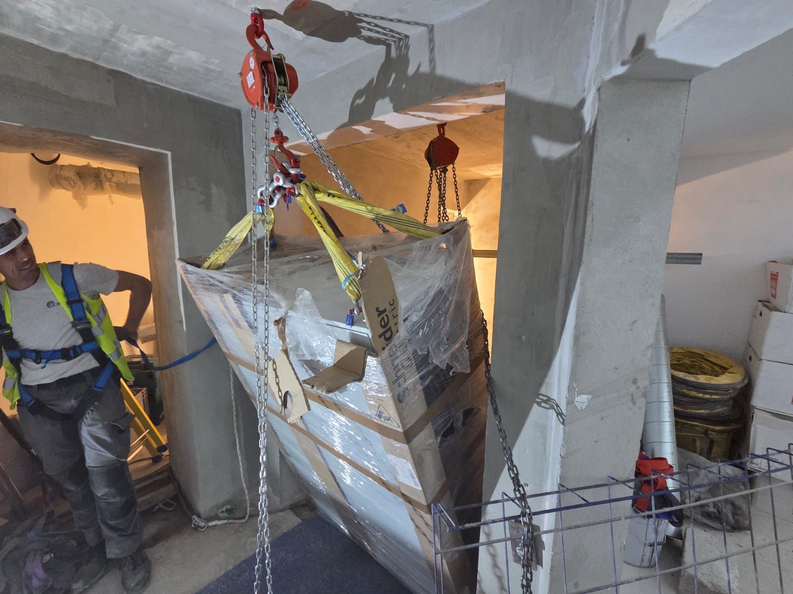 Un ouvrier en équipement de protection guide une palette emballée suspendue dans un espace de chantier intérieur étroit