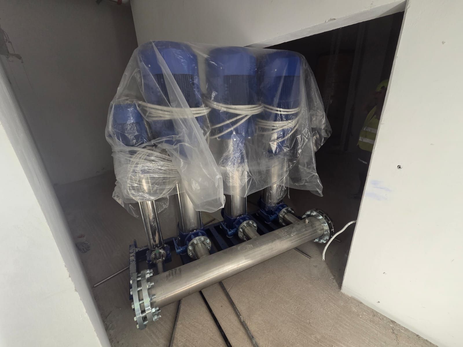 Chaises bleues emballées dans du plastique, près d’un grand ensemble de tuyaux métalliques dans une ouverture de porte