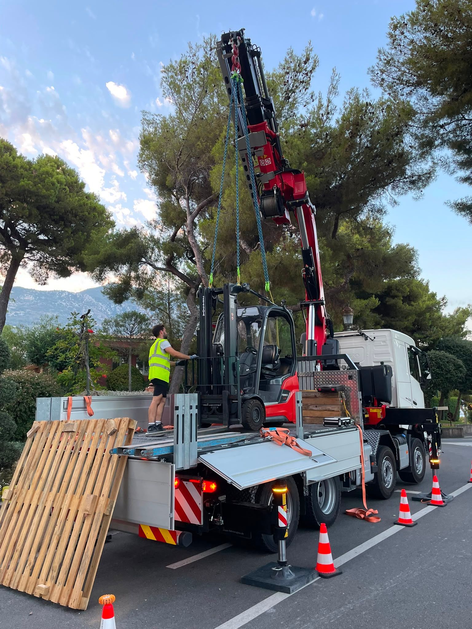 Camion-grue de dépannage avec une flèche rouge et des ouvriers qui installent des cônes de signalisation près des arbres