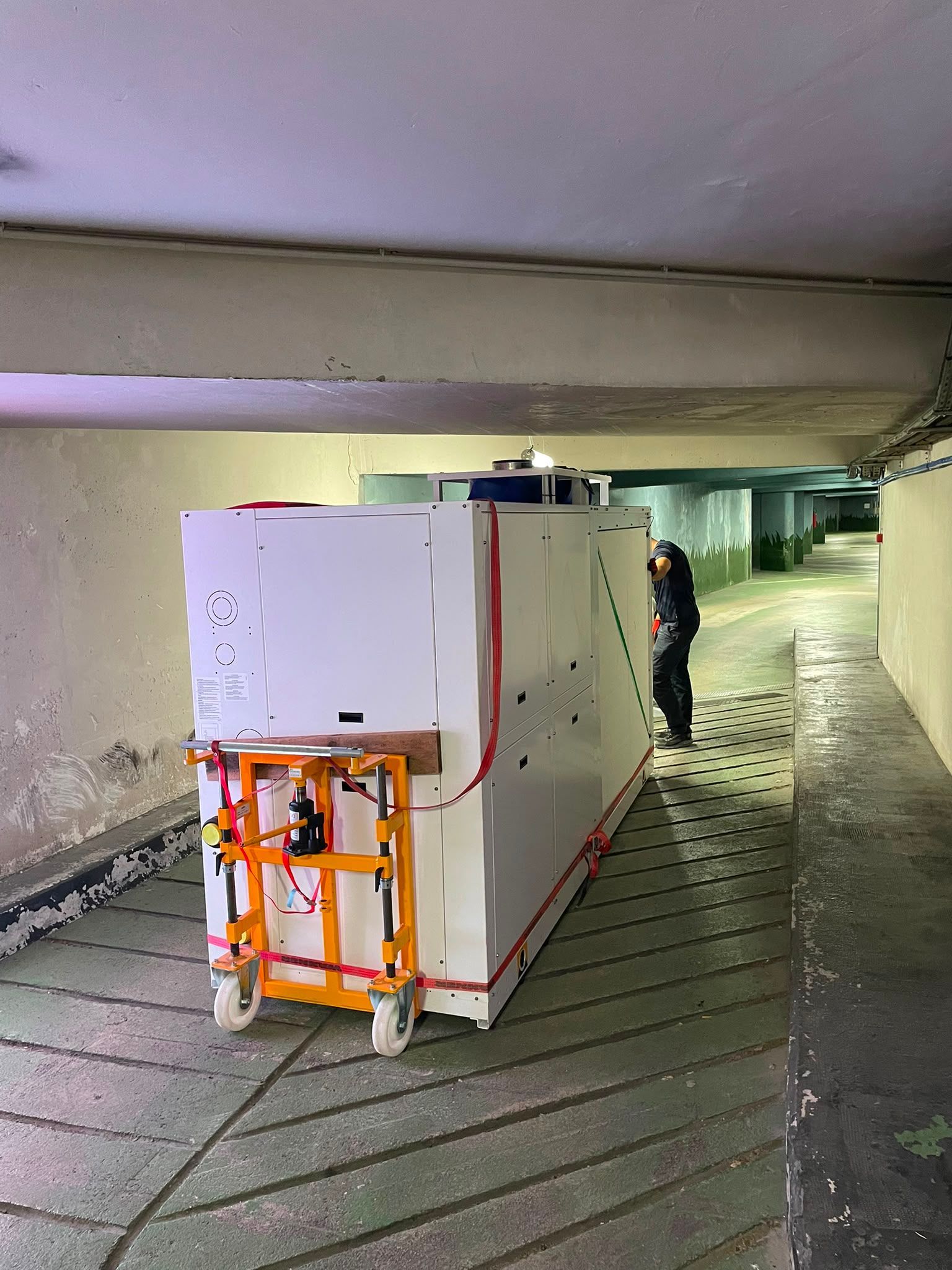 Grand chariot utilitaire blanc avec un cadre orange dans un parking couvert, avec une personne à proximité.