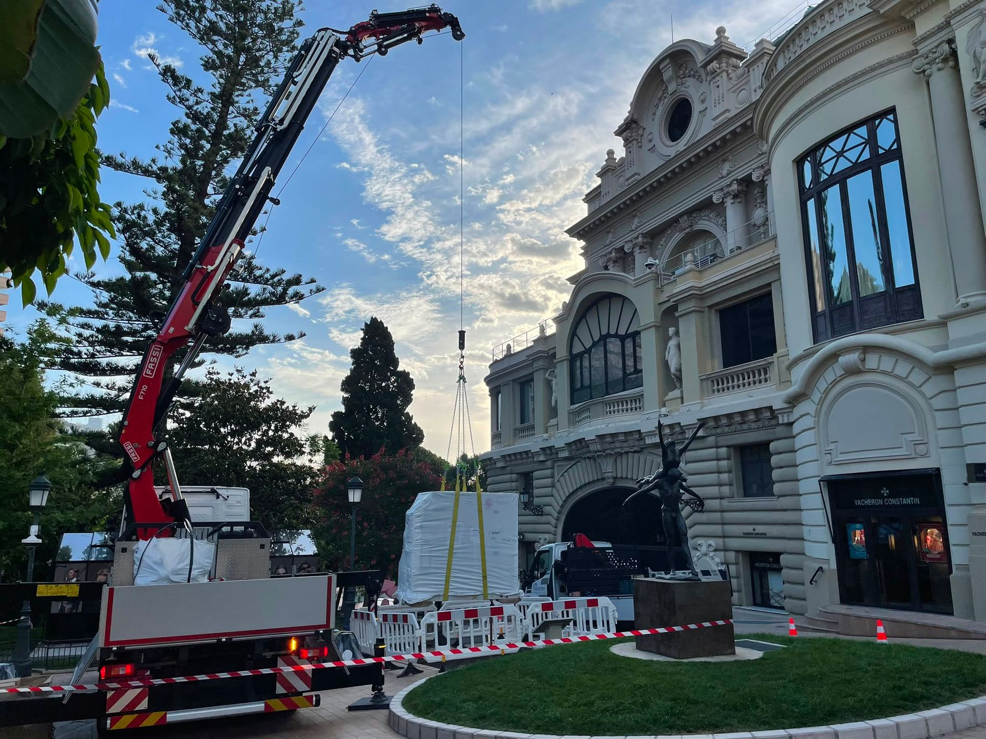 Un camion-grue soulève un grand sapin de Noël près d’un bâtiment historique orné, au crépuscule