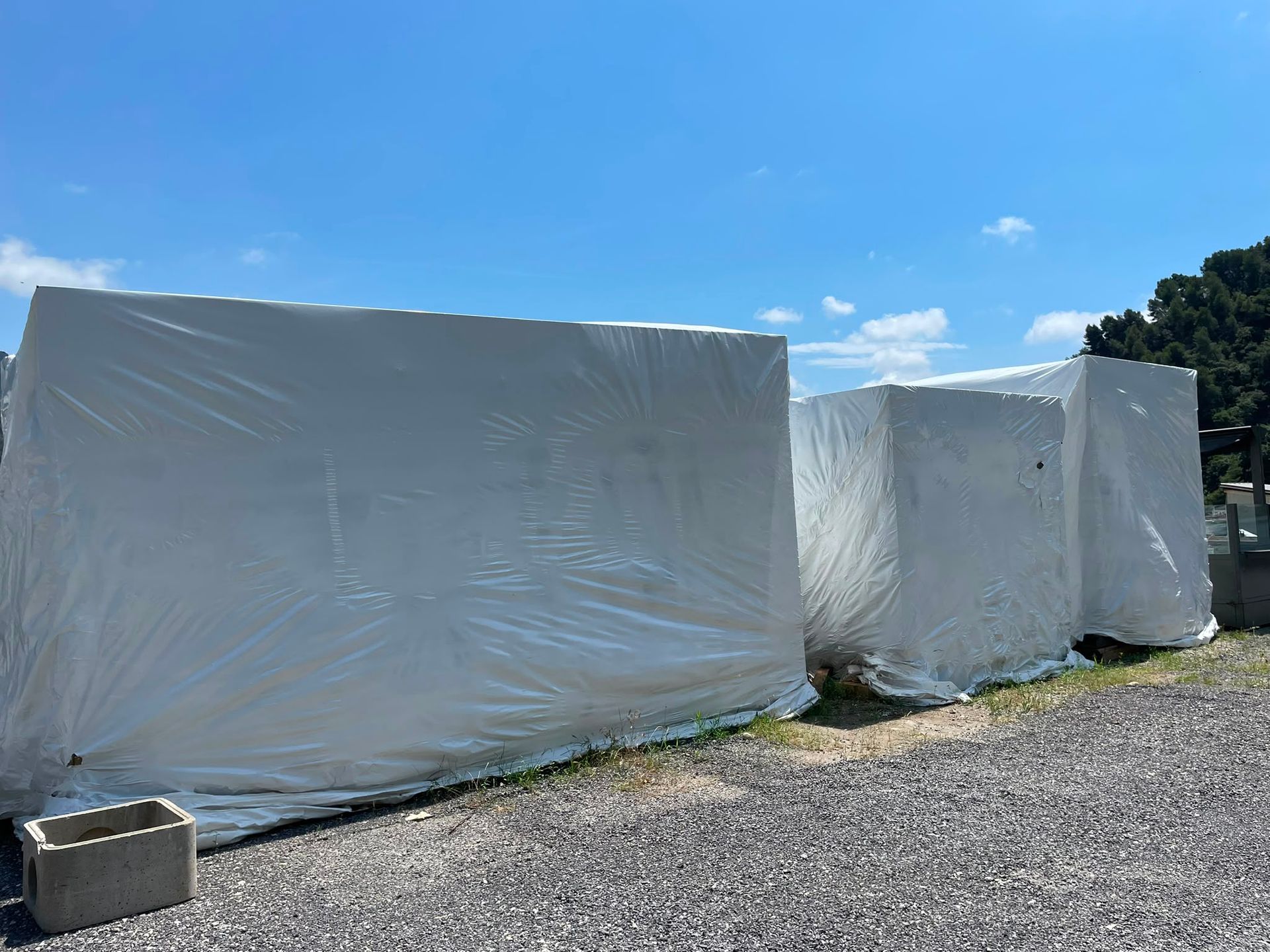 De grands objets rectangulaires emballés de blanc sont posés sur un terrain gravillonné sous un ciel bleu.