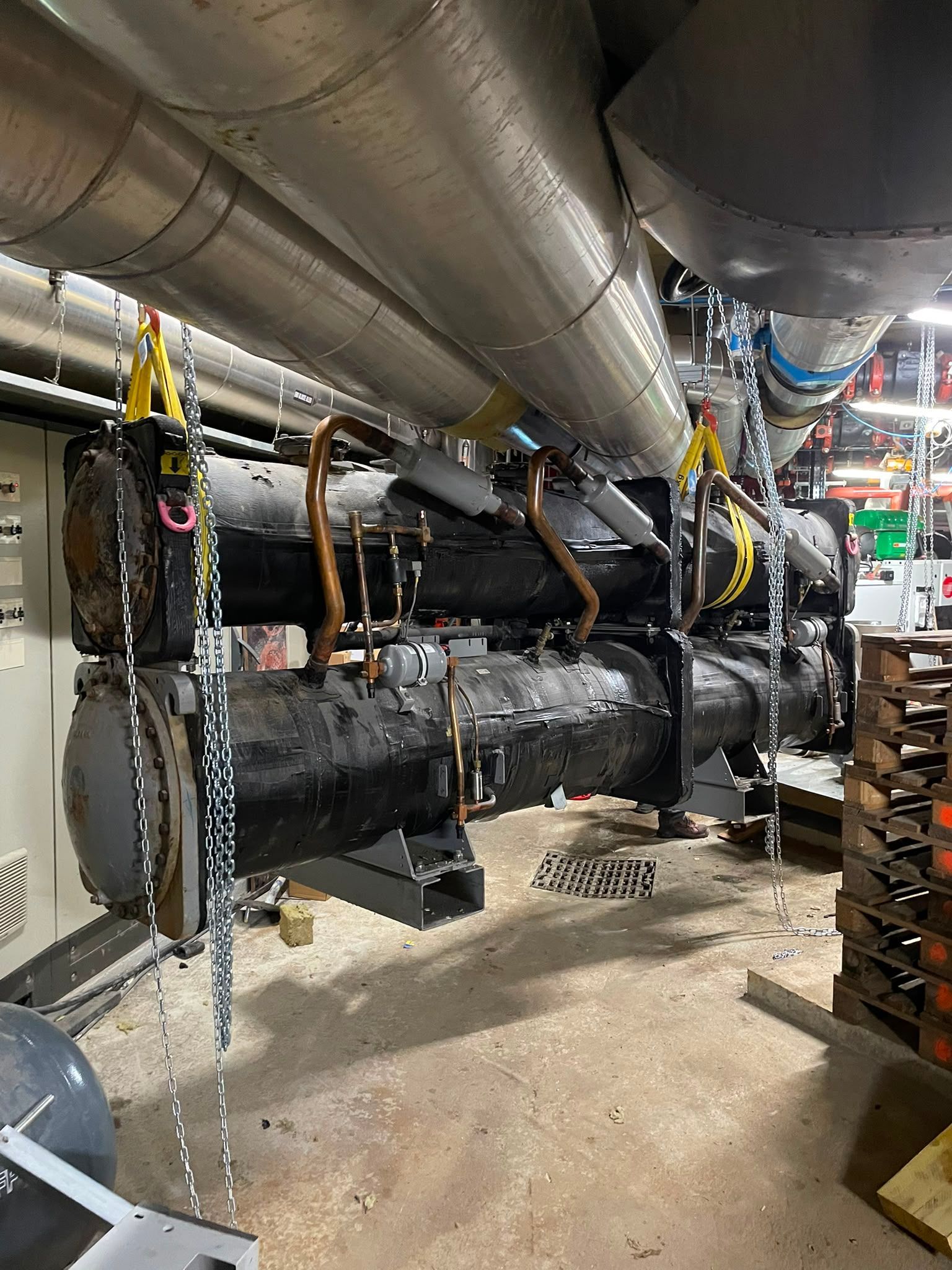 Sous-sol industriel avec une grosse conduite noire enveloppée d’isolant et des gaines en hauteur, maintenue par des sangles jaunes