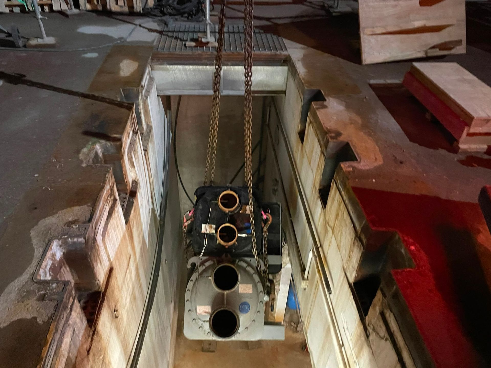 Compartiment moteur abaissé dans la coque d’un navire à l’aide d’un palan à chaîne, dans un atelier industriel