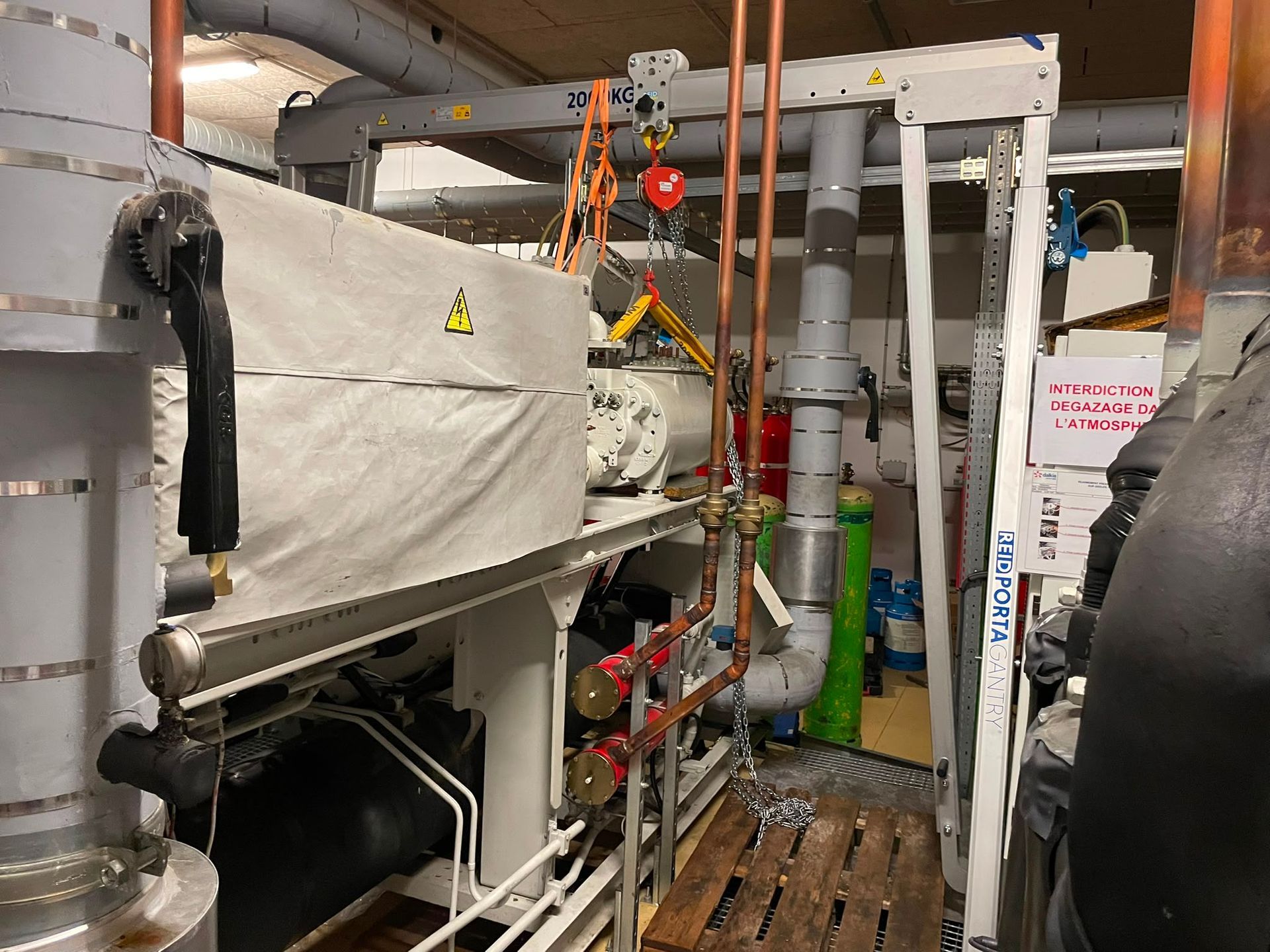 Des machines industrielles et des tuyaux dans un local technique, avec des vannes et un appareil recouvert.