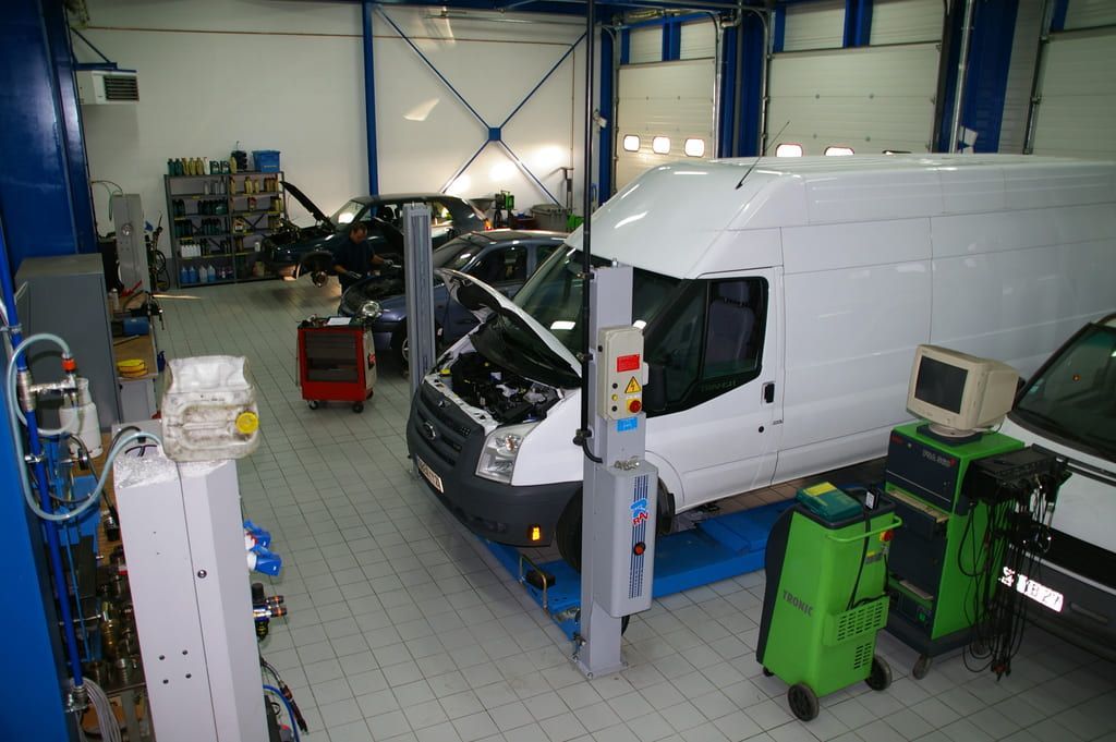 Une camionnette dans un garage automobile, capot ouvert, entourée d'outils et d'équipements