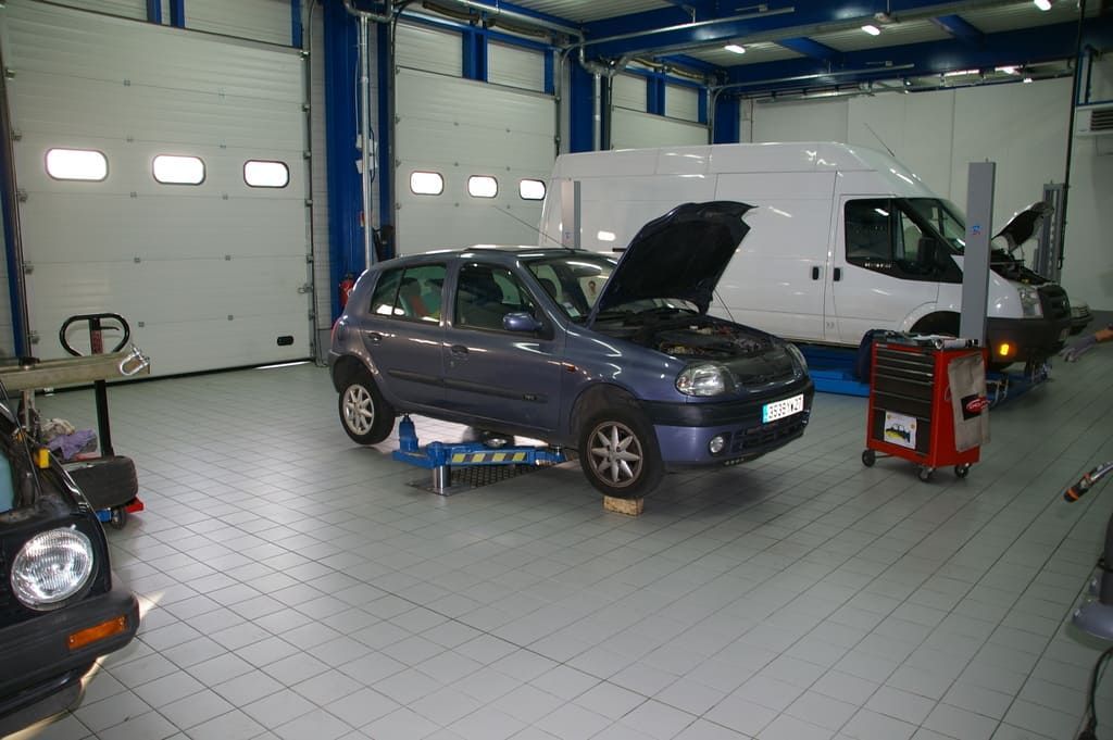 Voiture dans un garage, capot ouvert, entourée d'outils et d'équipements.