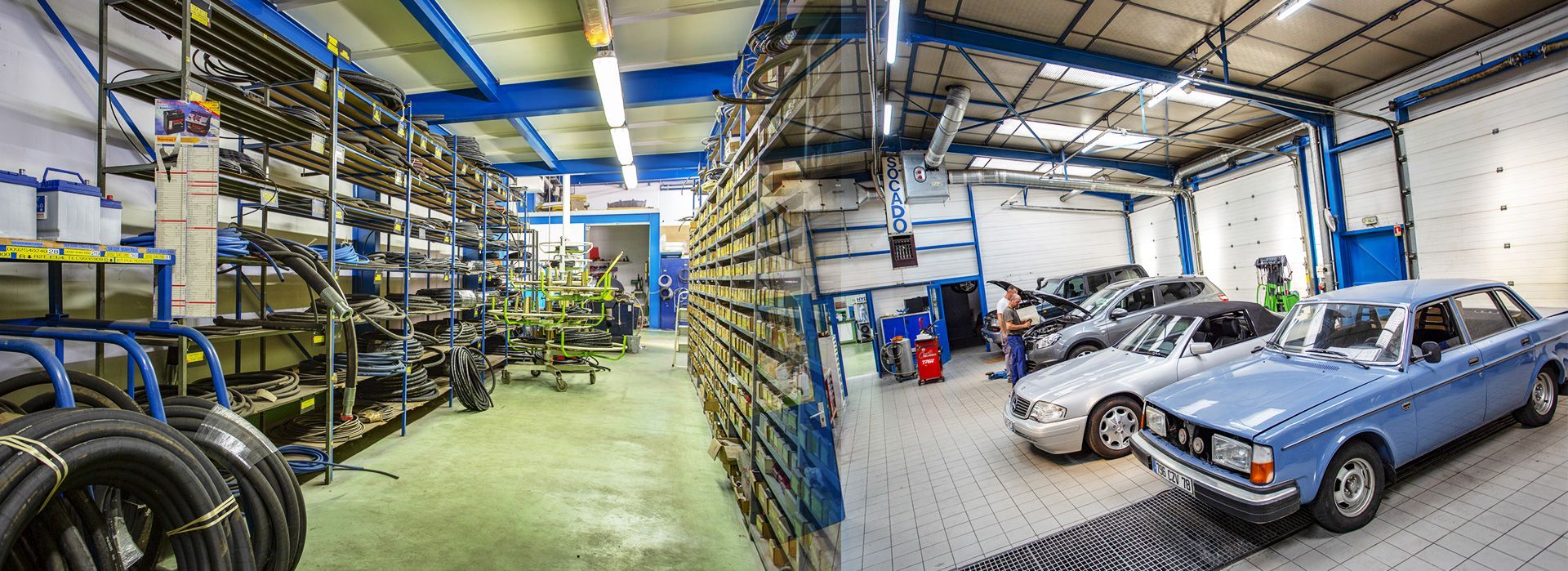 Garage de réparation automobile avec une voiture bleue, des outils, des étagères et deux personnes travaillant à l'intérieur