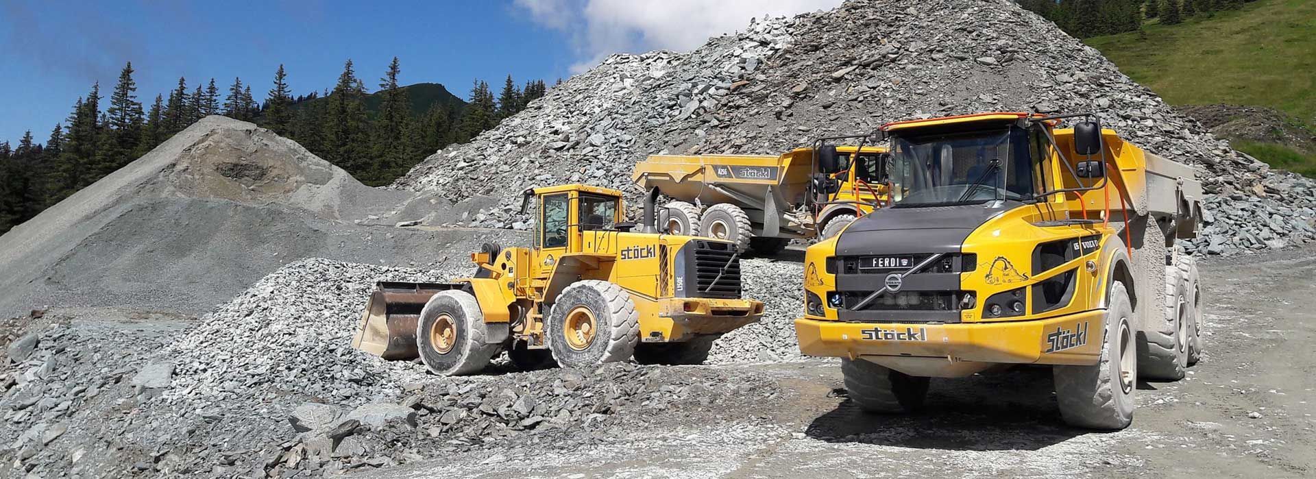 Chargeuses de chantier jaunes et camion-benne dans une gravière, avec des tas de roches en arrière-plan