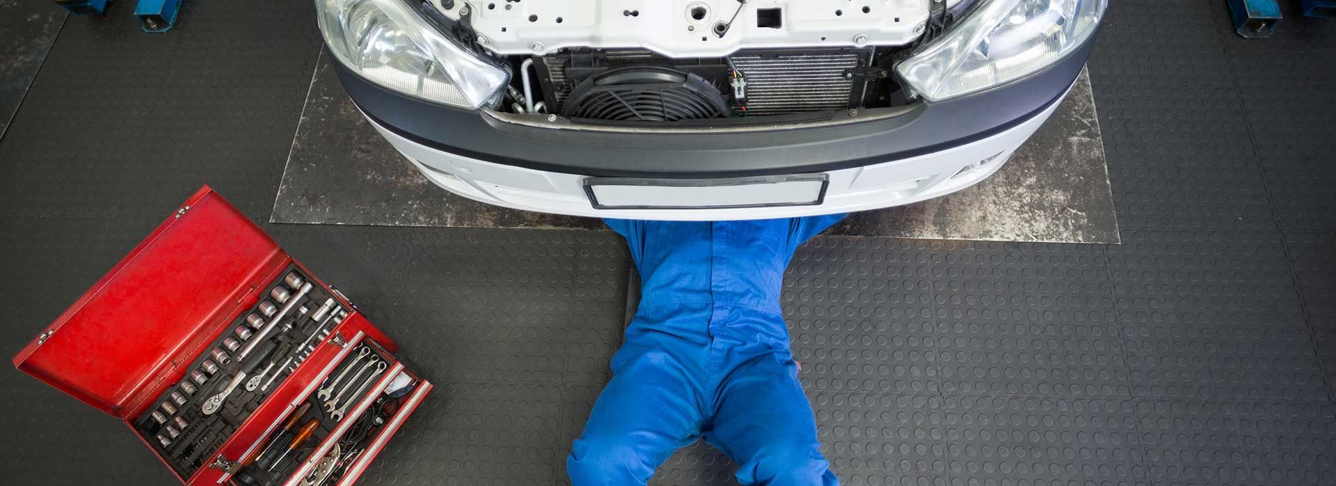 Un mécanicien sous une voiture surélevée, avec une boîte à outils rouge posée à proximité.