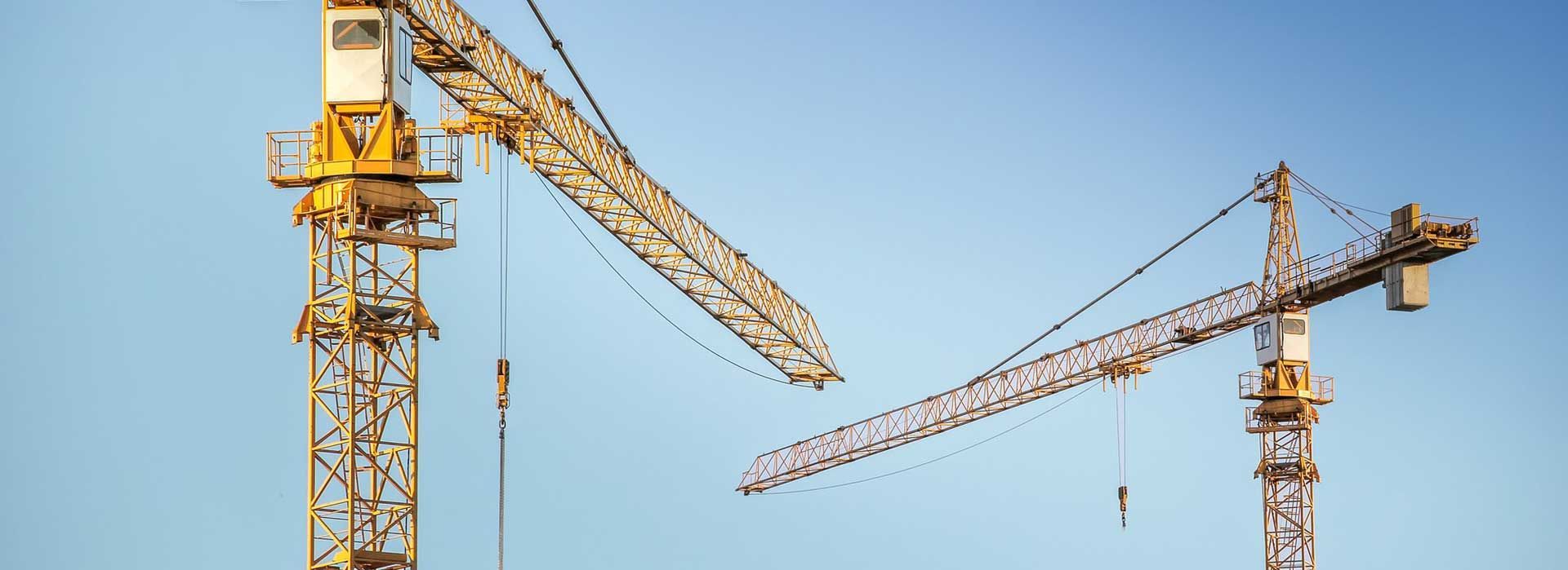 Deux grues de construction jaunes se détachant sur un ciel bleu clair