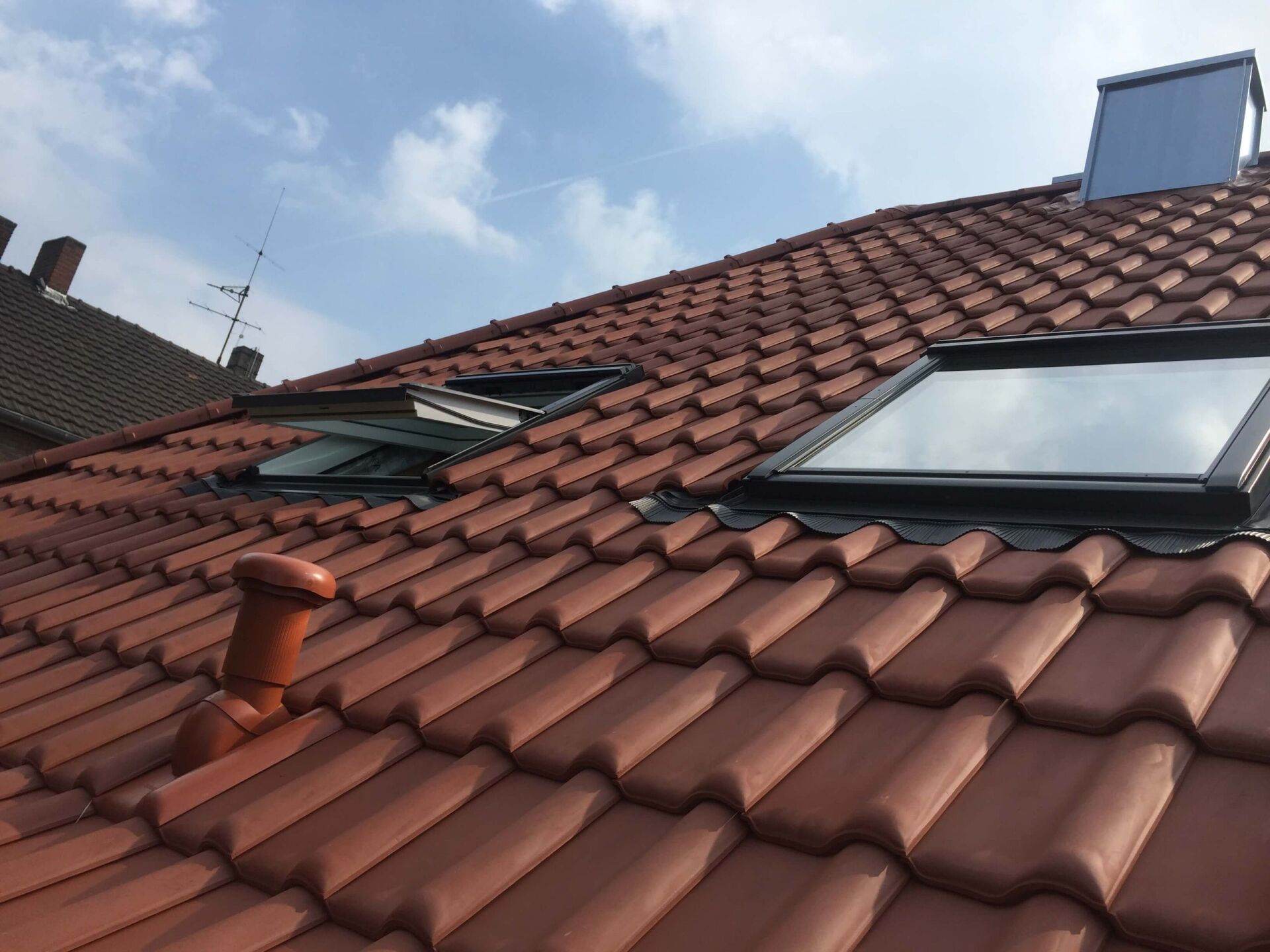 Rotes Ziegeldach mit Oberlichtern unter einem bewölkten Himmel