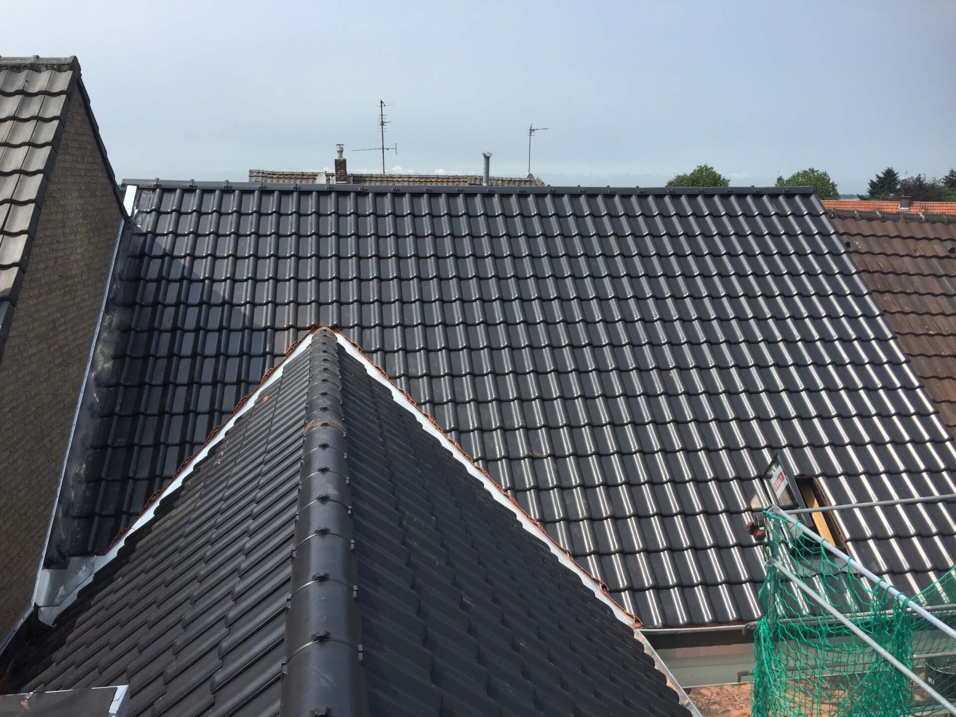 Dächer mit dunkelgrauen Ziegeln und einem grünen Baunetz vor blauem Himmel