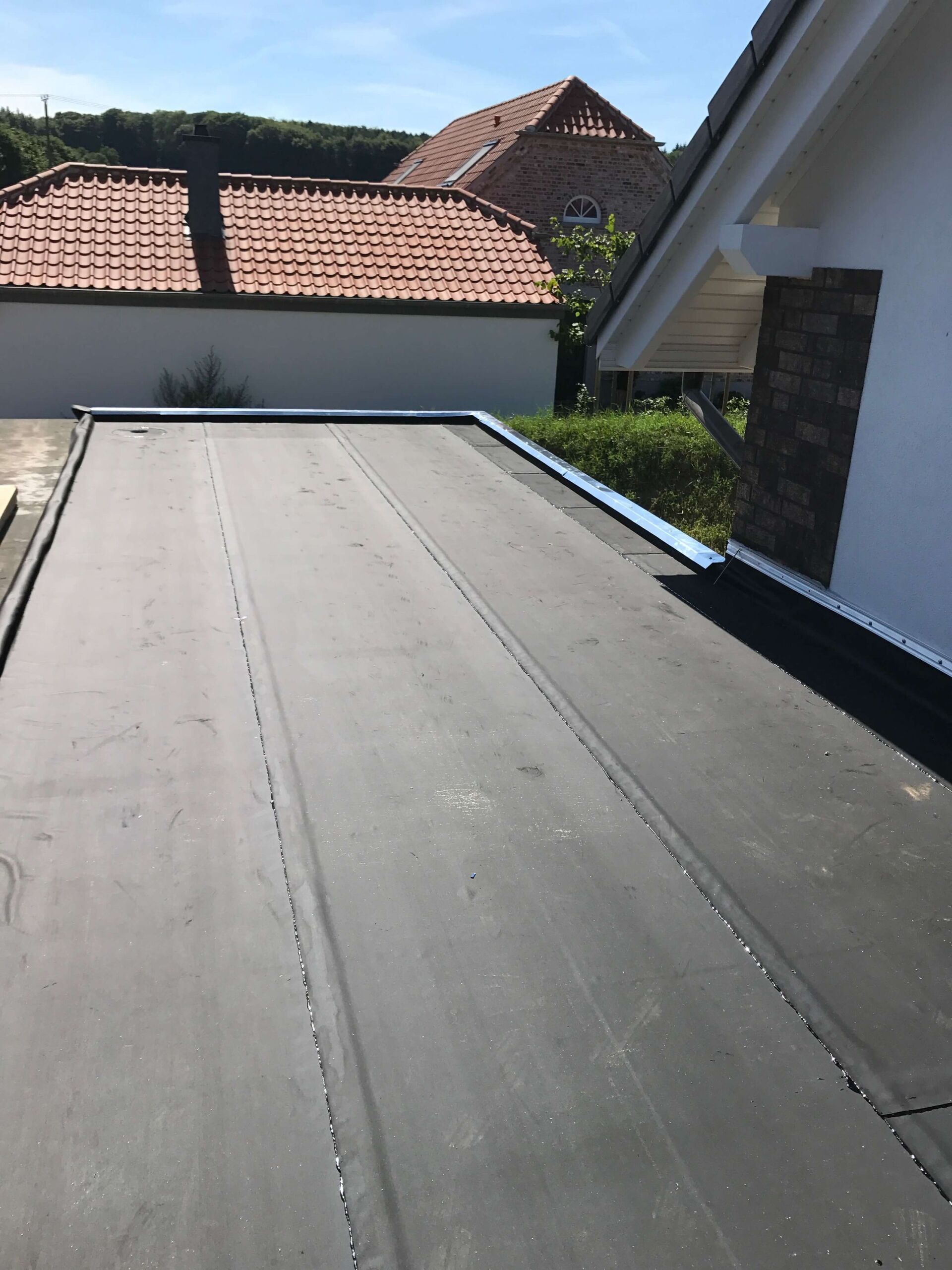 Flaches schwarzes Dach neben einem weißen Haus und rot gedeckten Gebäuden unter sonnigem Himmel