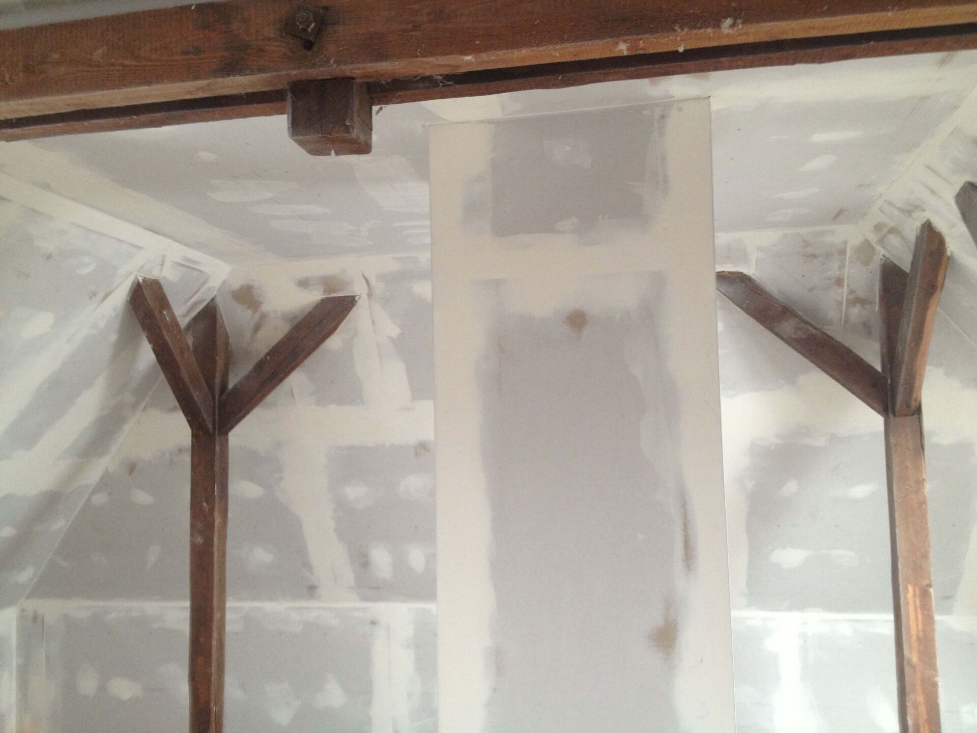 Innenwand mit freiliegenden Holzbalken und unfertiger Gipskartonwand um eine zentrale weiße Säule.
