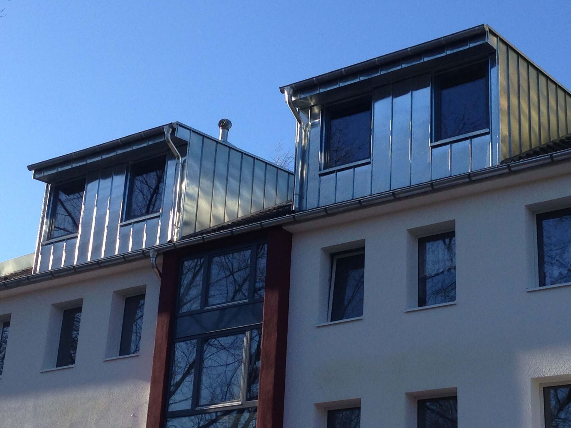 Modernes Wohnhaus mit Dachgauben aus Metall und blauem Himmel darüber
