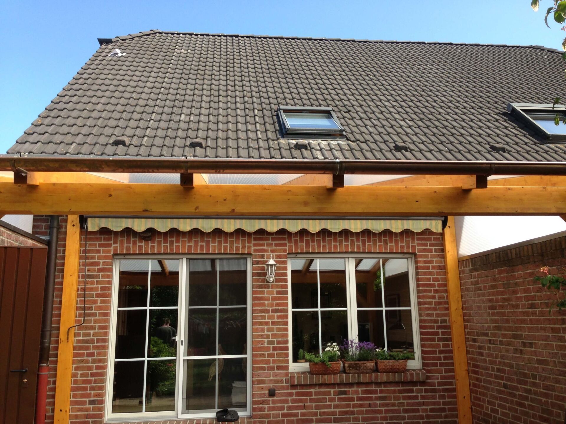 Backsteinhausfassade mit Ziegeldach, Oberlicht, Holzbalken und großen Fenstern unter blauem Himmel