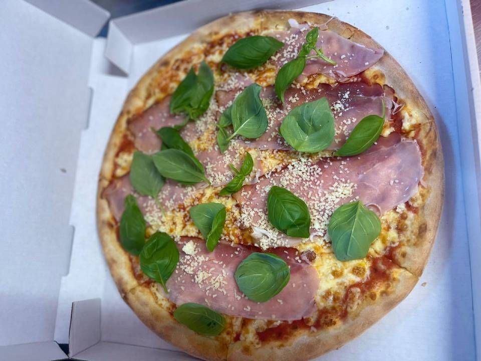 In einer Schachtel befindet sich eine Pizza mit Schinken, Spinat und Käse. Foto von EAT Point Laufen