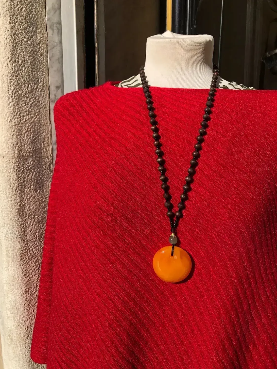 Un maniquí con un poncho rojo y un collar con un colgante naranja.