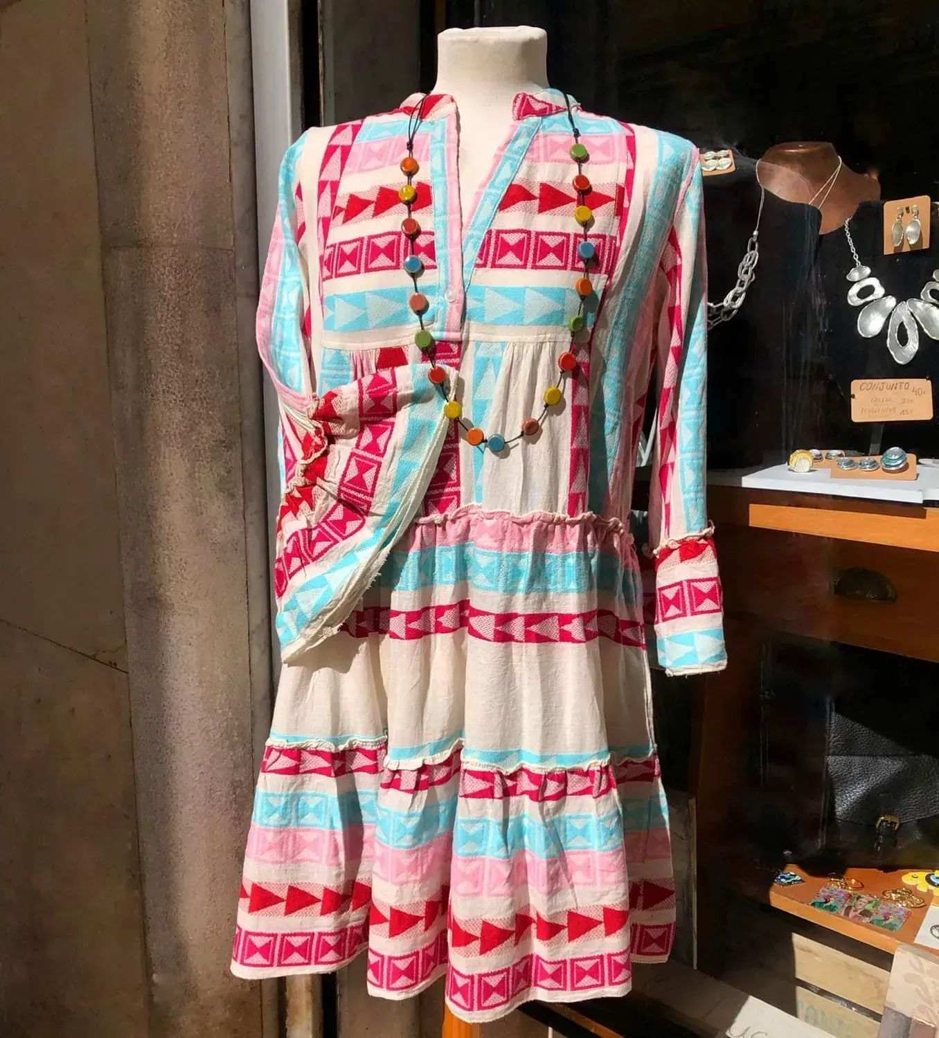 Un vestido colorido está en un maniquí frente a una ventana.