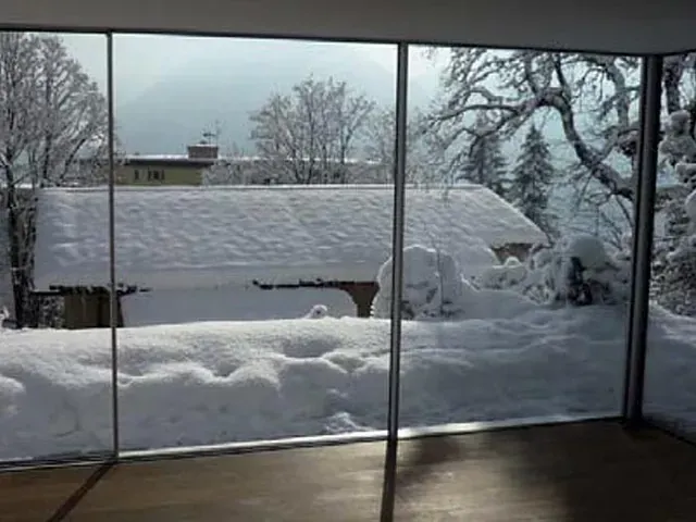 Una habitación con vista a un patio nevado a través de una ventana.